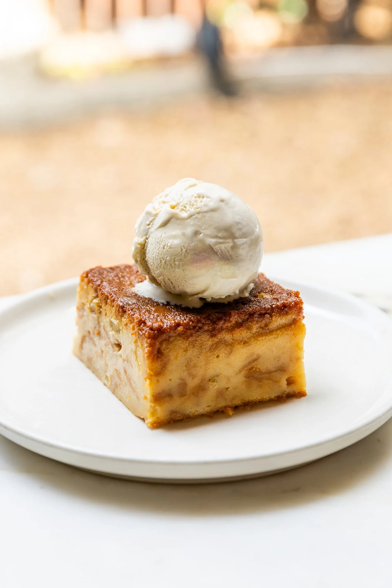 A square piece of apple crumble topped with a scoop of vanilla ice cream on a white plate. Ovenbird Restaurant in Birmingham, Alabama.