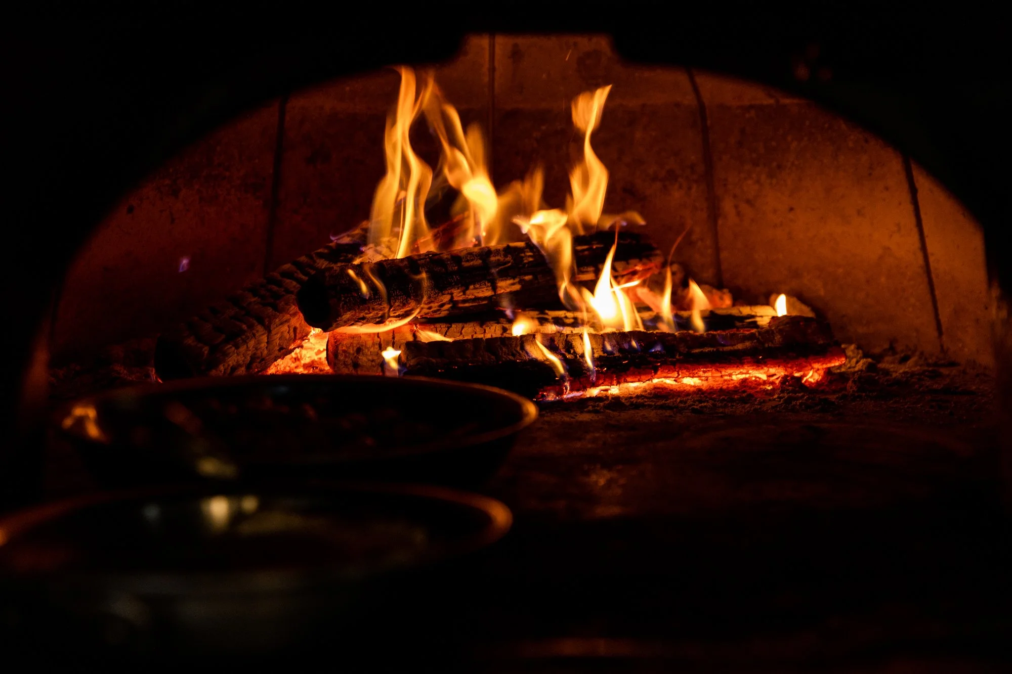 A close-up view of a wood fire burning in a fireplace, with orange and yellow flames, glowing embers, and bricks in the background. Hot andHot Fish Club Restaurant in Birmingham, Alabama.