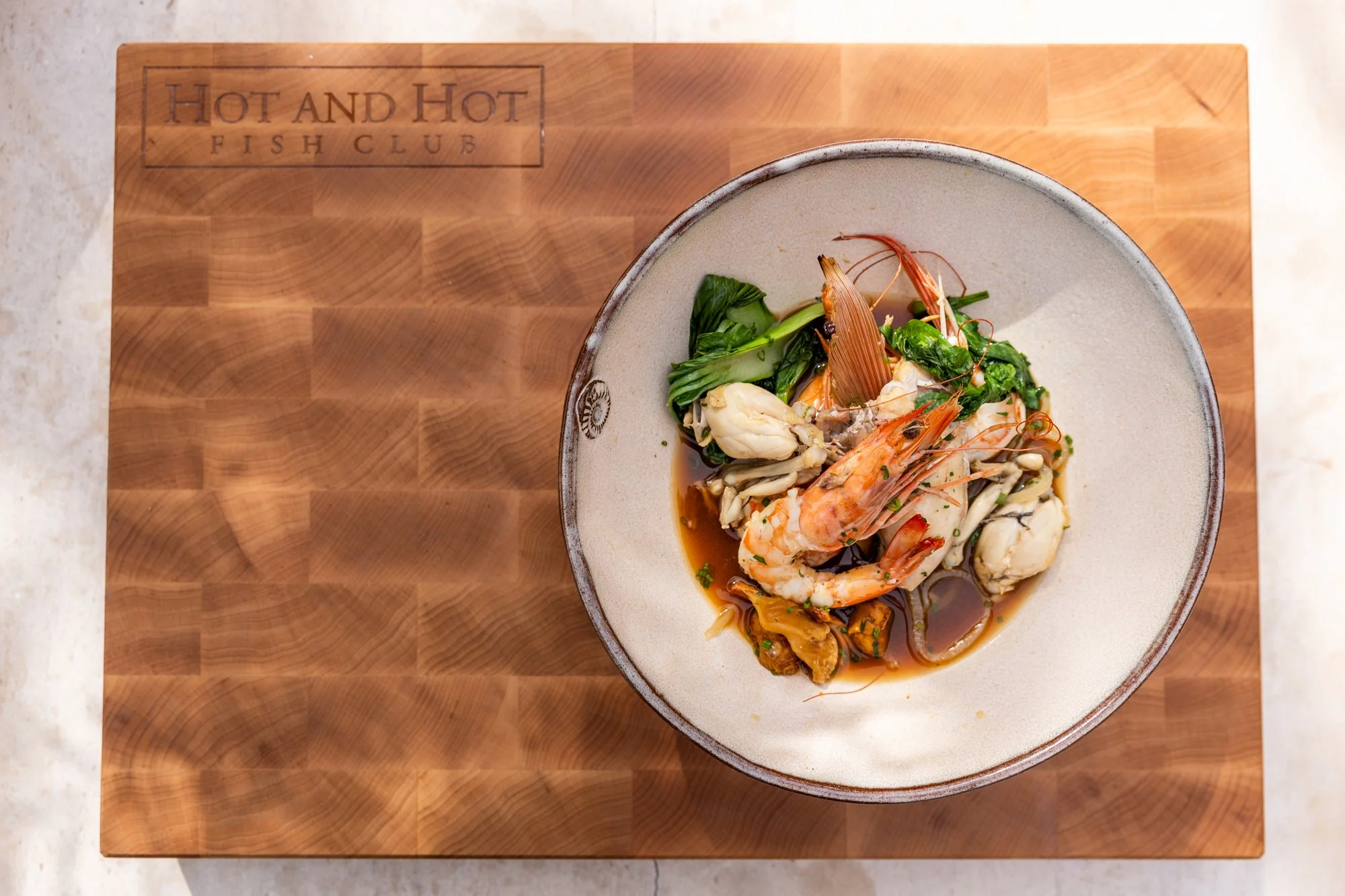 Seafood dish with shrimp, clams, and greens served in a bowl on a wooden board Hot and Hot Fish Club Restaurant in Birmingham, Alabama.