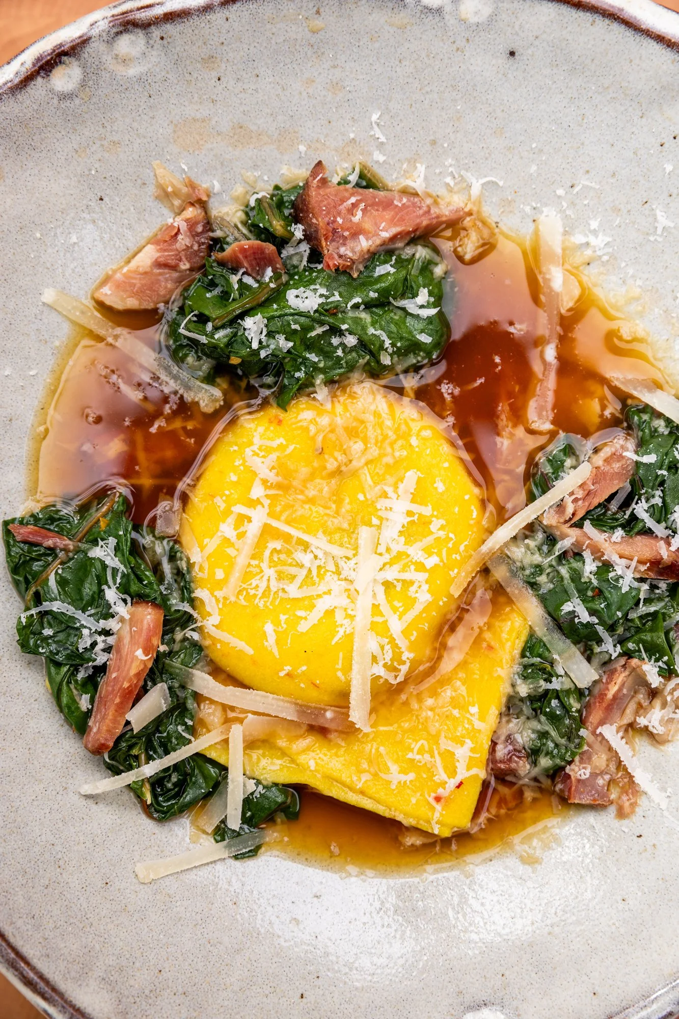 Eggs cooked sunny side up with spinach, shaved cheese, ham, and sauce in a bowl. Hot and Hot Fish Club Restaurant in Birmingham, Alabama.