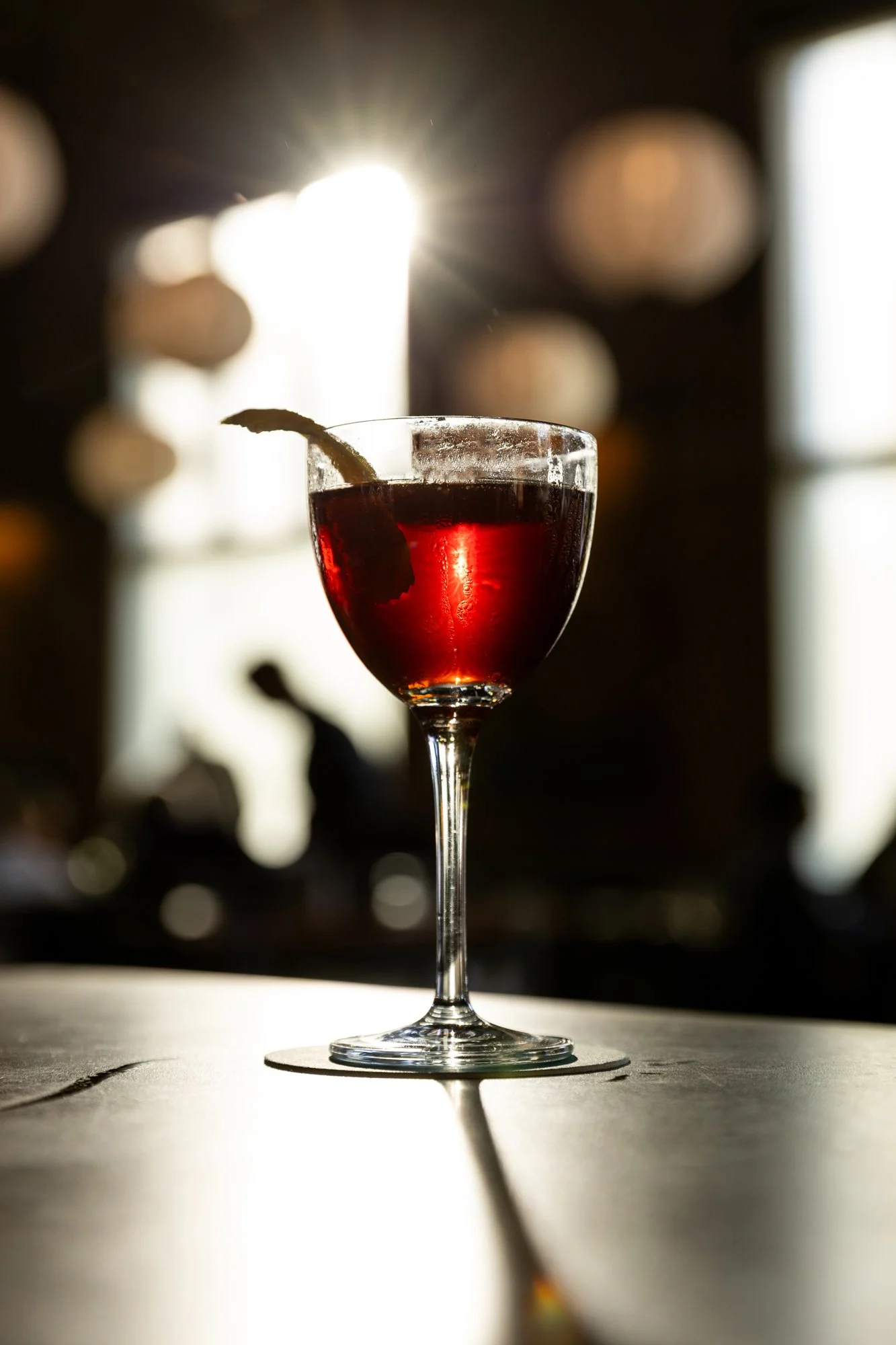 A glass of red wine on a table with sunlight shining through it, creating a glow and reflection on the surface.