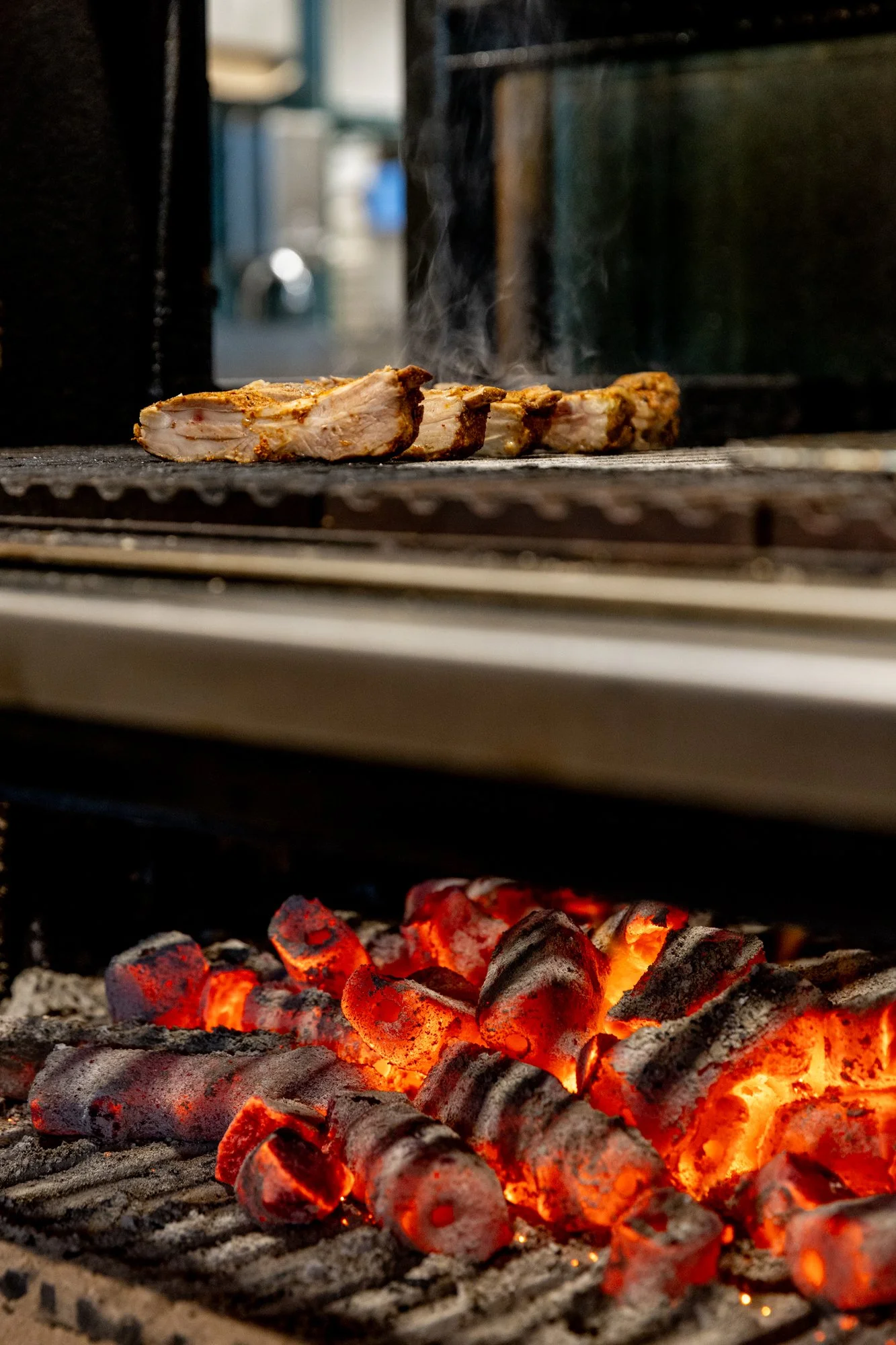 barbecue grill with red hot charcoal at the bottom and pieces of meat cooking on the top rack