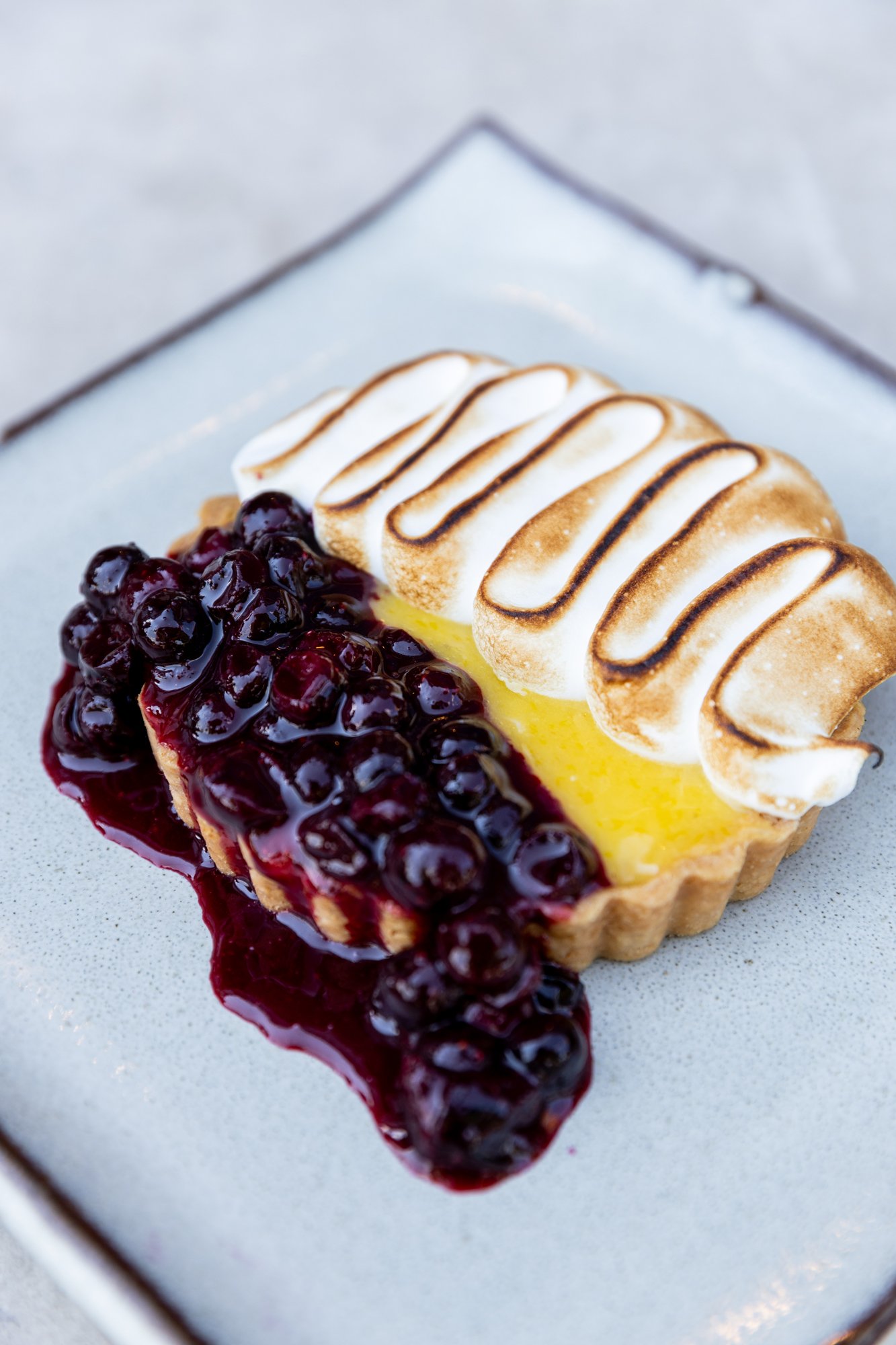 Lemon tart with blueberry compote and toasted meringue topping on a white plate Hot and Hot Fish Club Restaurant in Birmingham, Alabama.