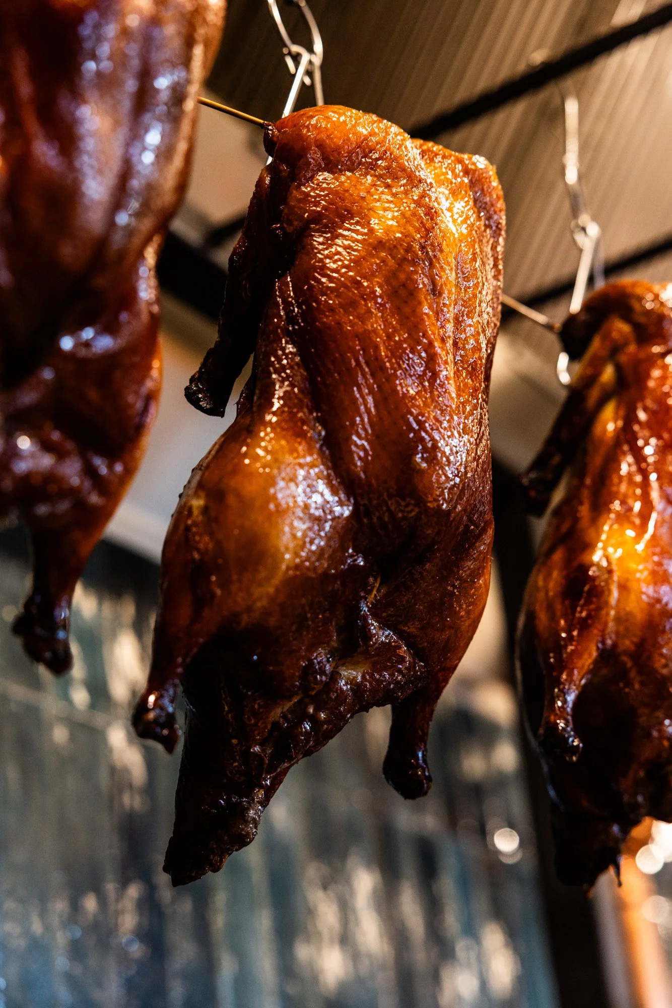 Roasted whole ducks hanging from hooks in a restaurant kitchen.