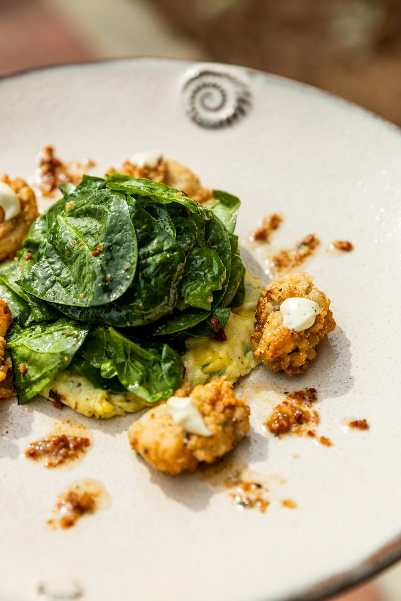 A plate of food with fresh greens, fried chicken pieces, and a creamy sauce. Hot and Hot Fish Club Restaurant in Birmingham, Alabama.