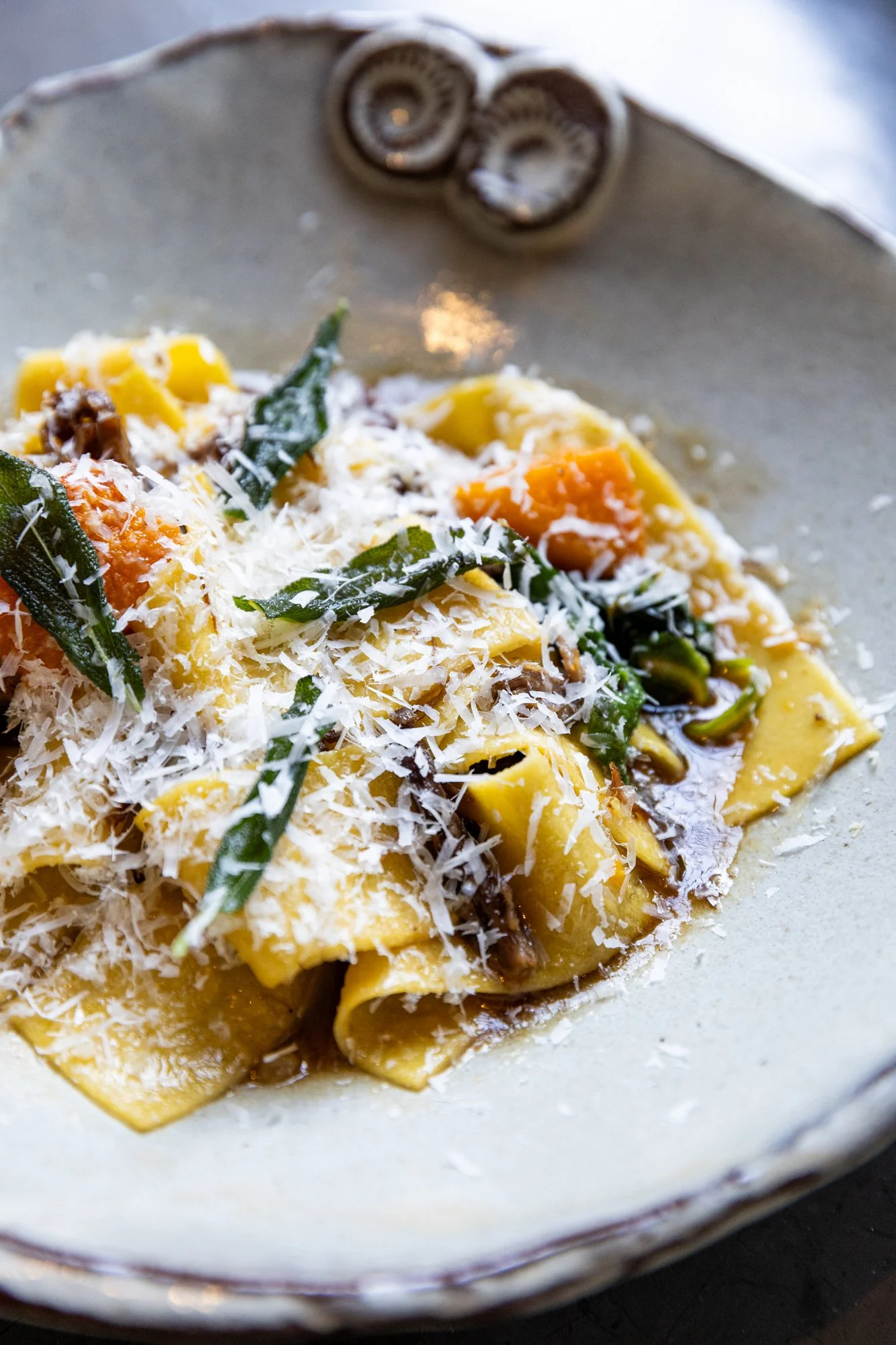 Close-up of a plate of cooked pasta with grated cheese, green herbs, and vegetables in a creamy sauce. Hot and Hot Fish Club Restaurant in Birmingham, Alabama.