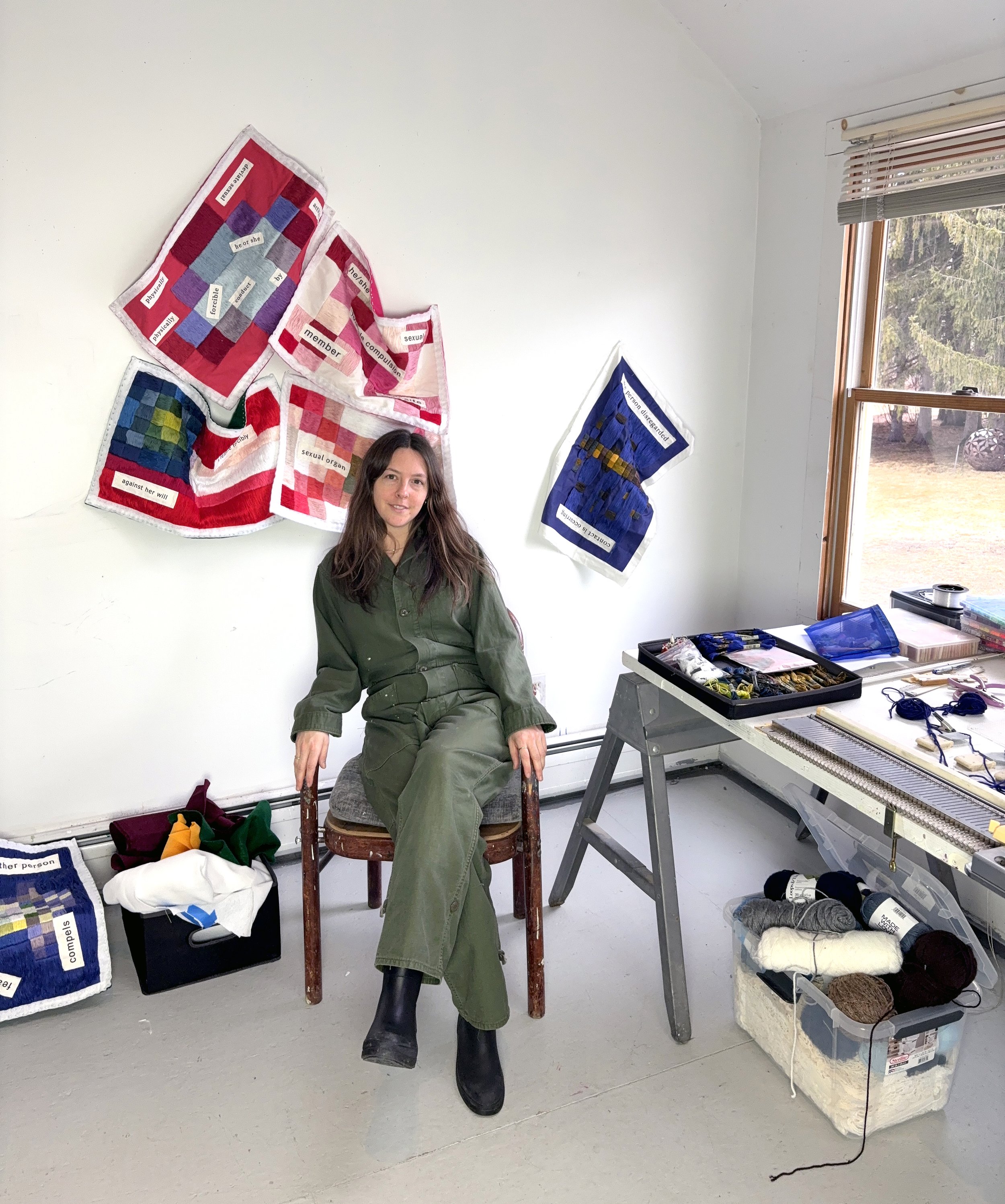 Woman in a green jumpsuit with brown hair sitting in her art studio