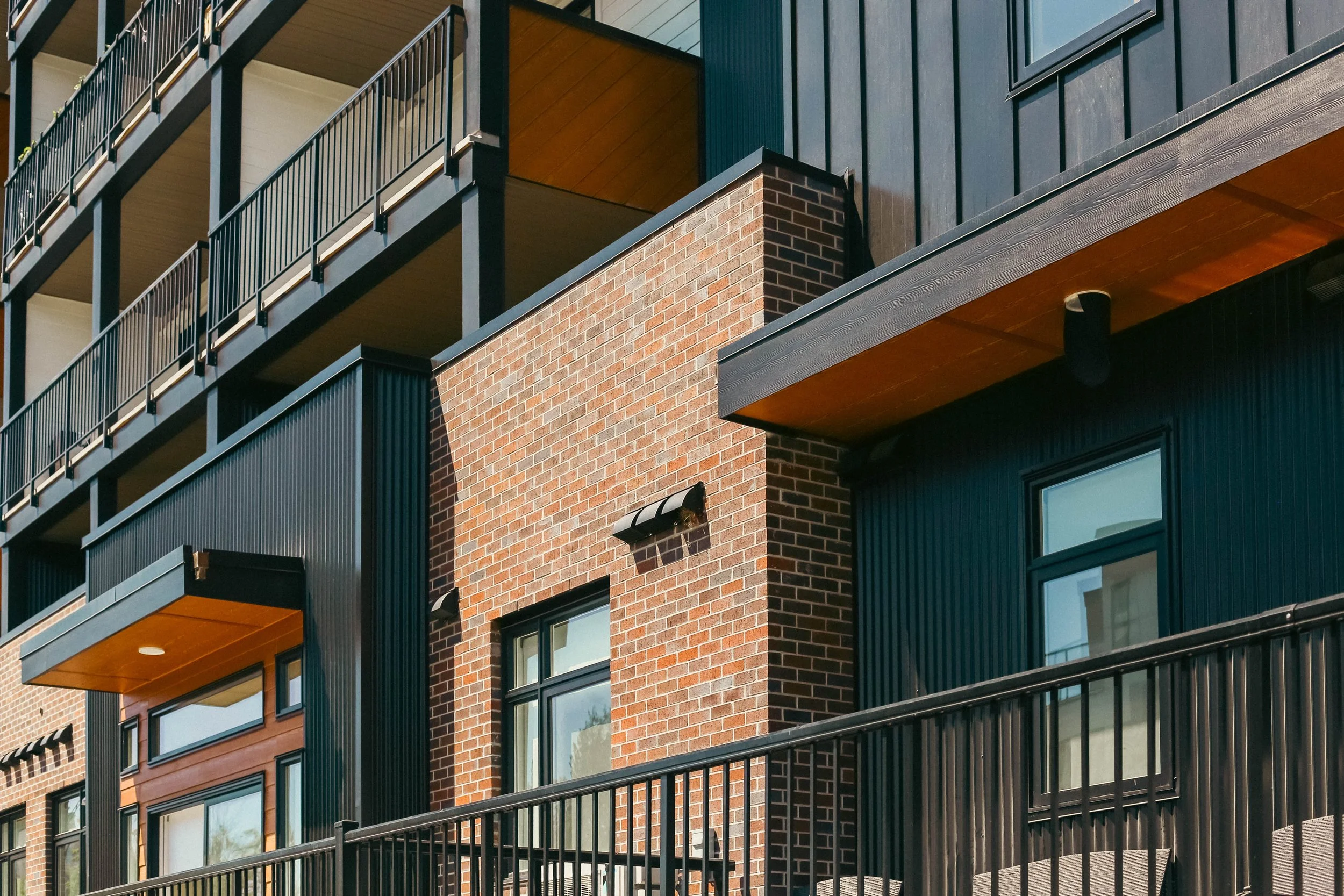 Multifamily building exterior with brick, dark cladding, balcony railings and black-framed windows