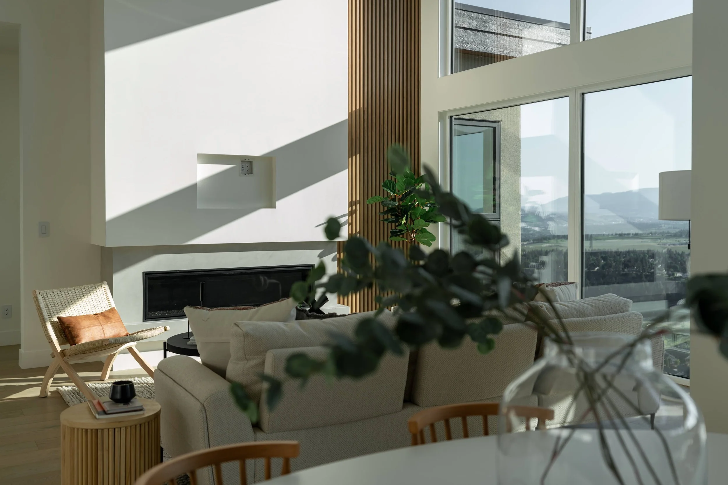 Double-height living room with a linear fireplace, wood slat feature and tall windows, Trailhead Showhome, Kelowna