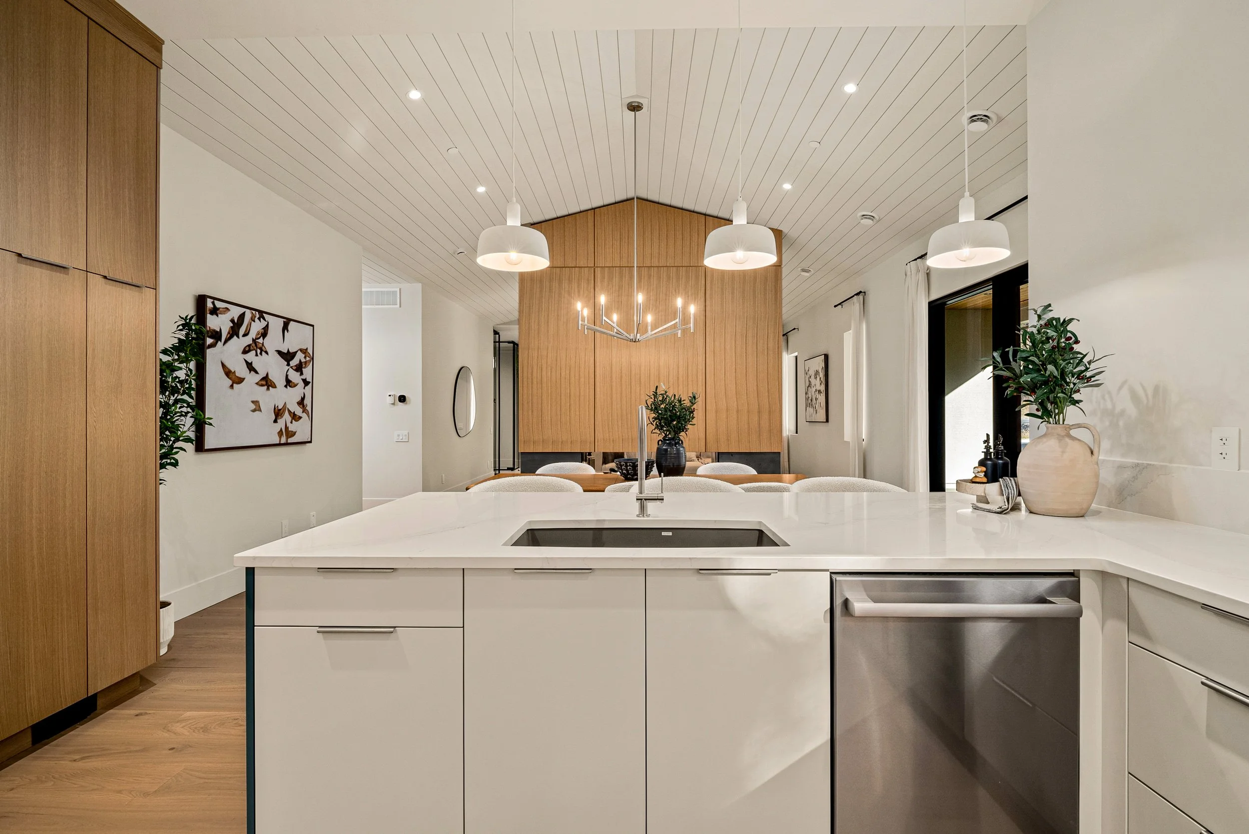 Open main floor at Woodside Showhome — kitchen island looking through to the wood fireplace wall that ties living, dining, and kitchen