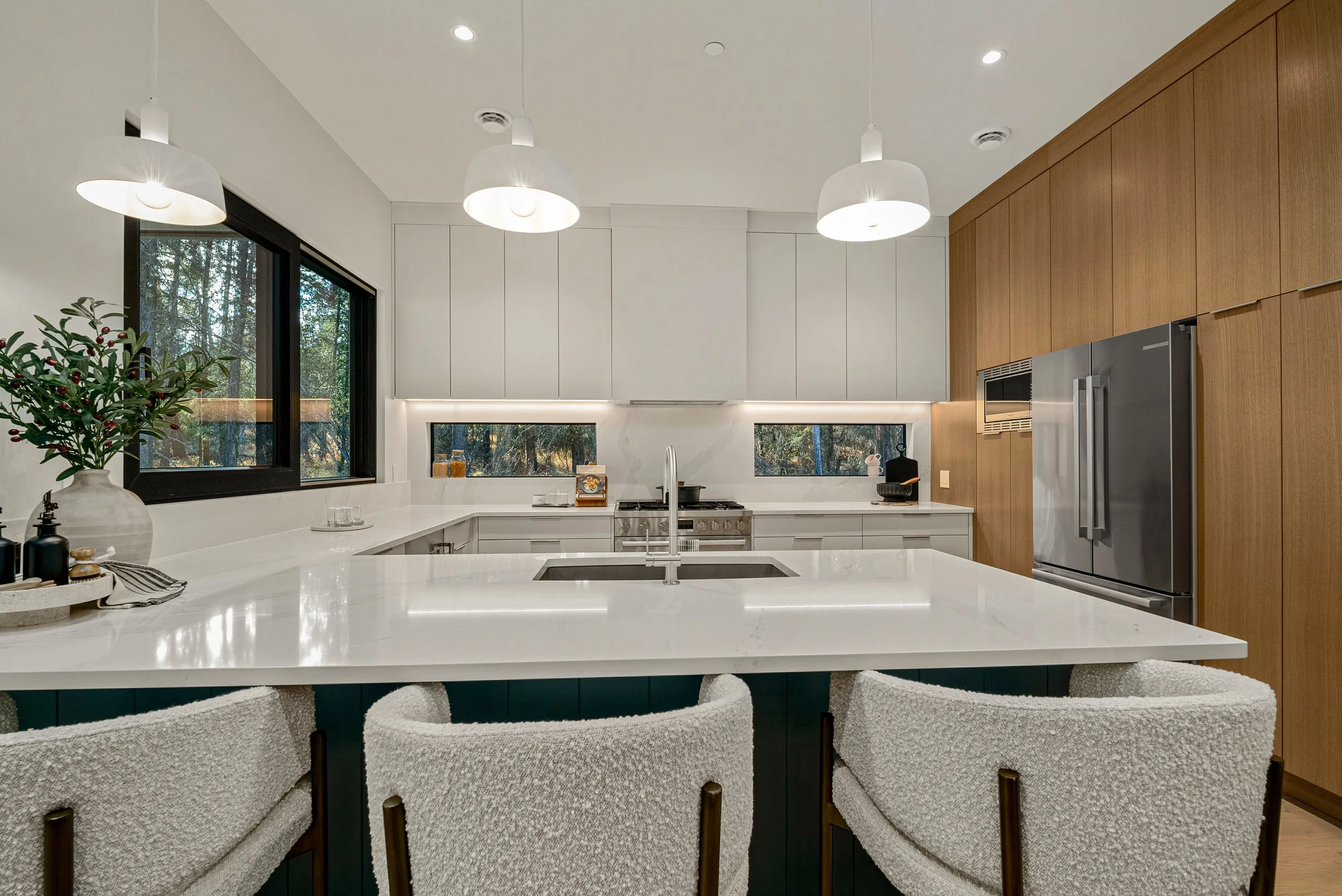 Woodside Showhome kitchen with forest-green island, white stone, bouclé stools, and ribbon windows to the trees