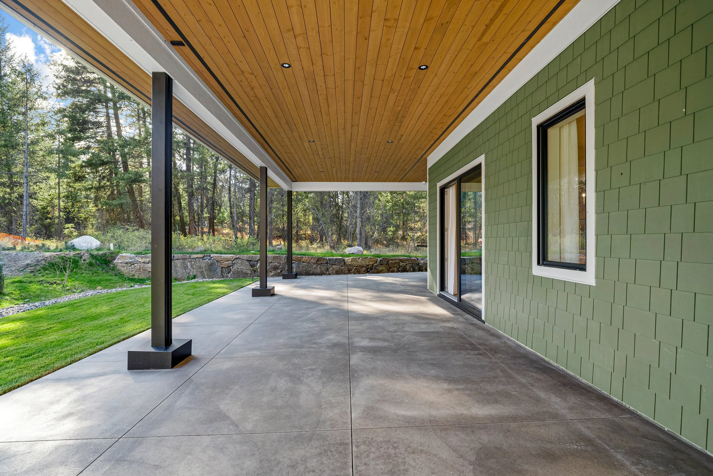 Covered patio at Woodside Showhome — wood soffit, sage shingle, and forest edge at Predator Ridge