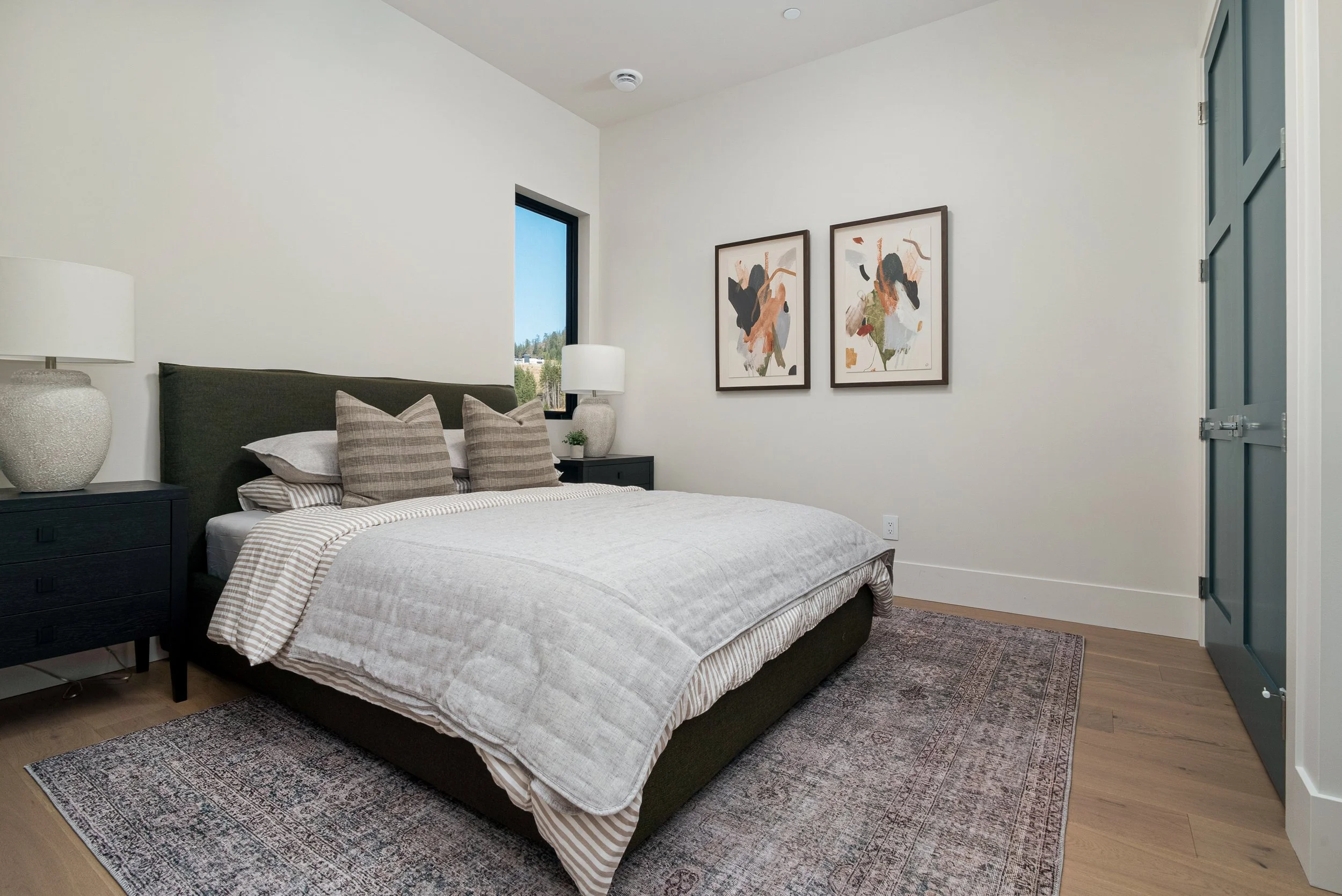 Woodside Showhome bedroom with a dark upholstered bed, striped pillows, a pair of abstract prints and a vintage-style rug