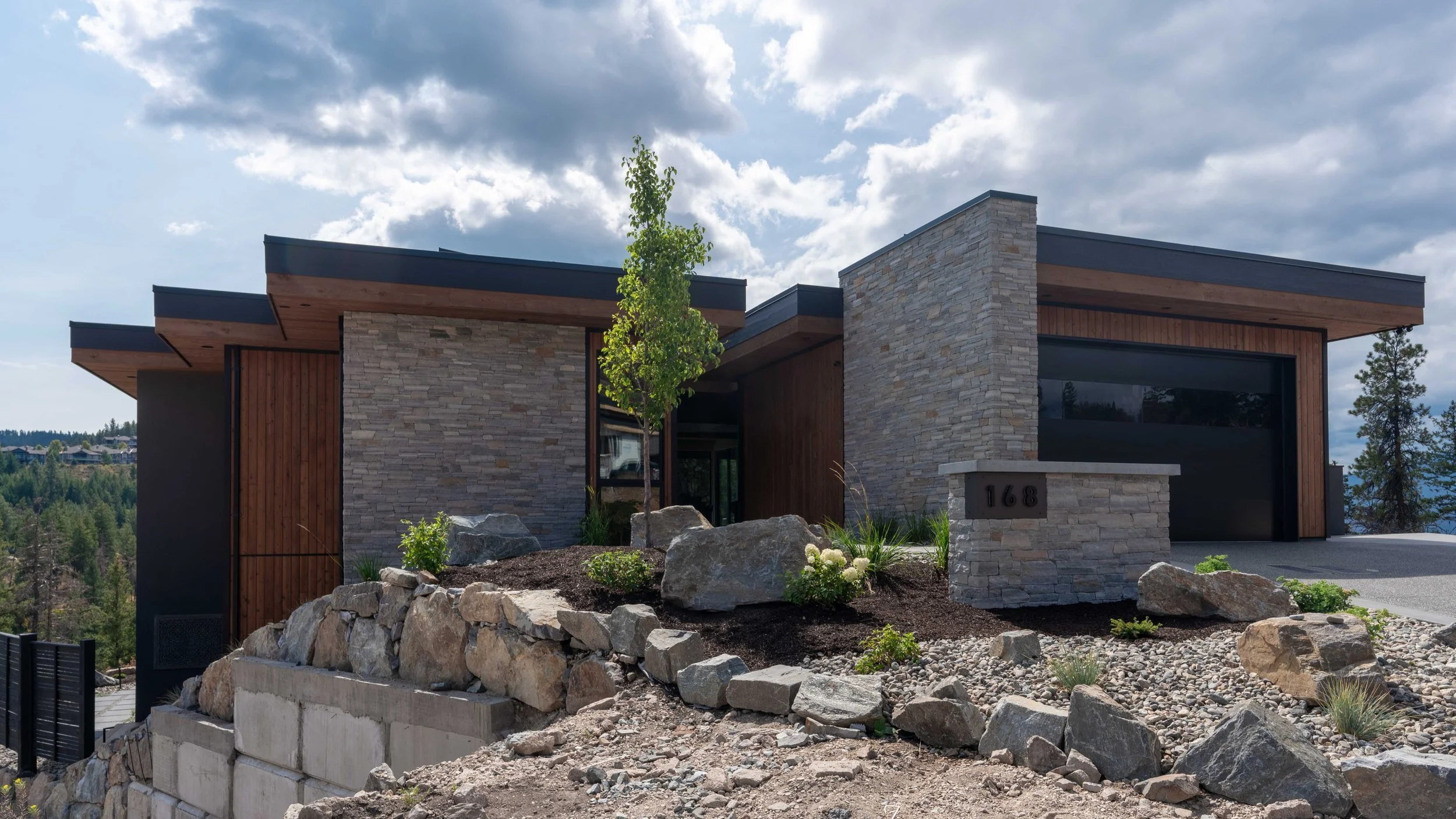 Ridge Light House exterior at Predator Ridge with stacked stone, wood siding, flat roofs and boulder landscaping