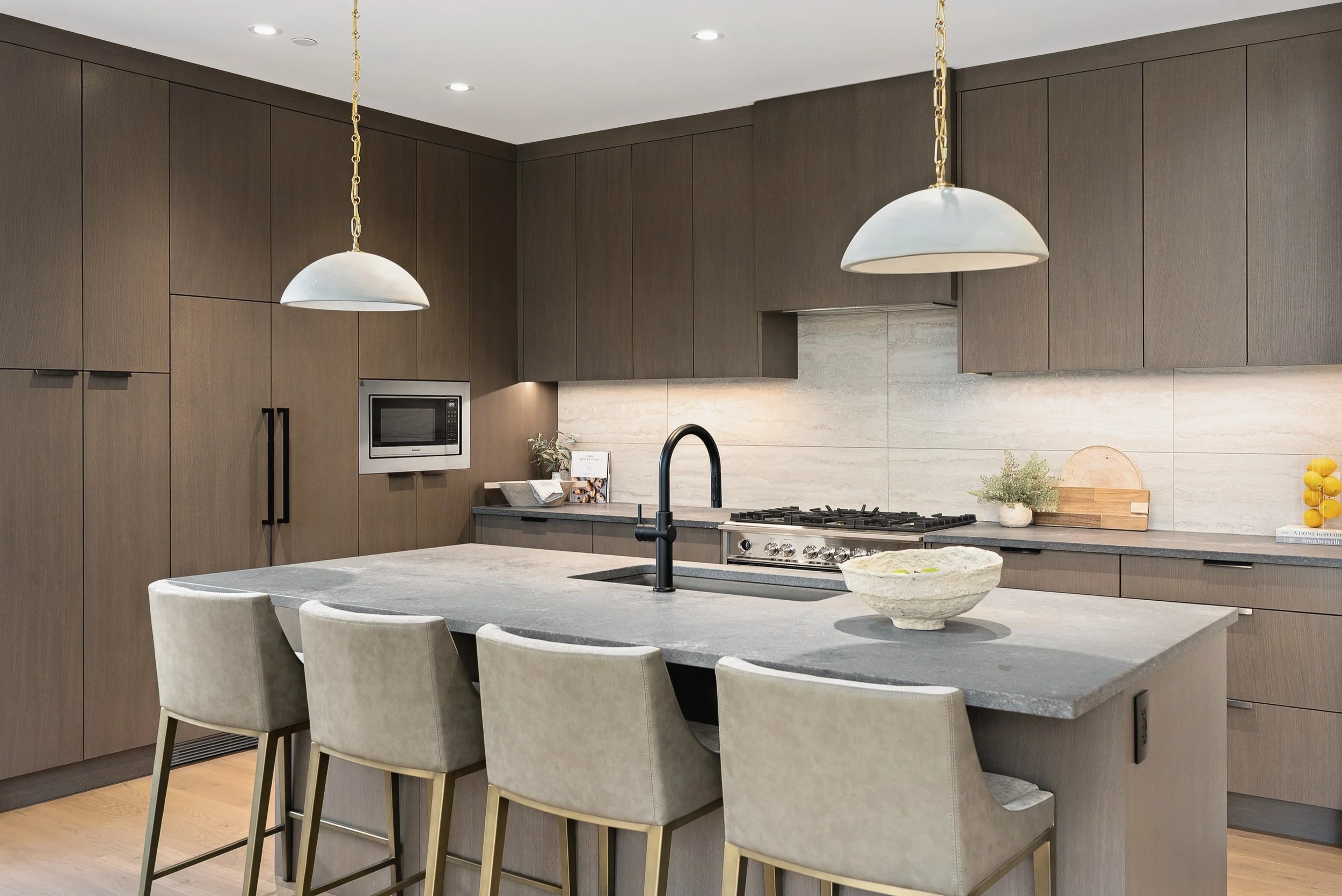Kitchen with dark oak cabinetry, a honed quartz island and white pendants, Green View Residence, Predator Ridge
