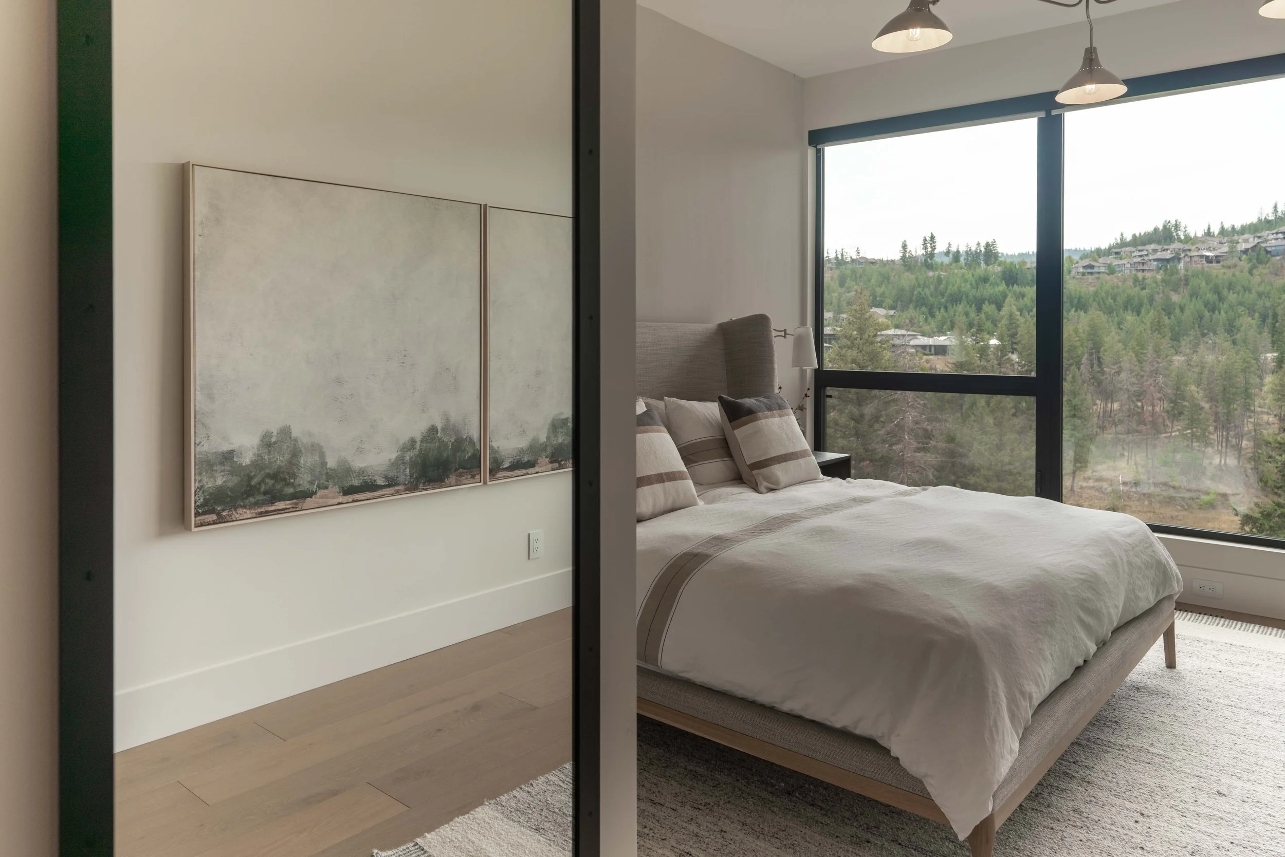 Bedroom at Ridge Light House with an upholstered bed, framed landscape art and corner windows to the forest