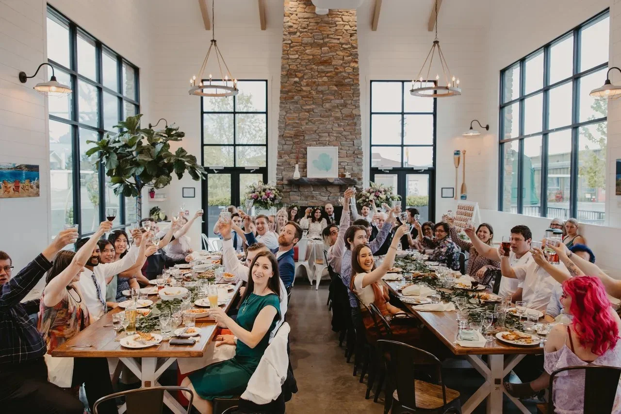 Brewery event space with a stone fireplace wall, tall black-framed windows and long communal tables