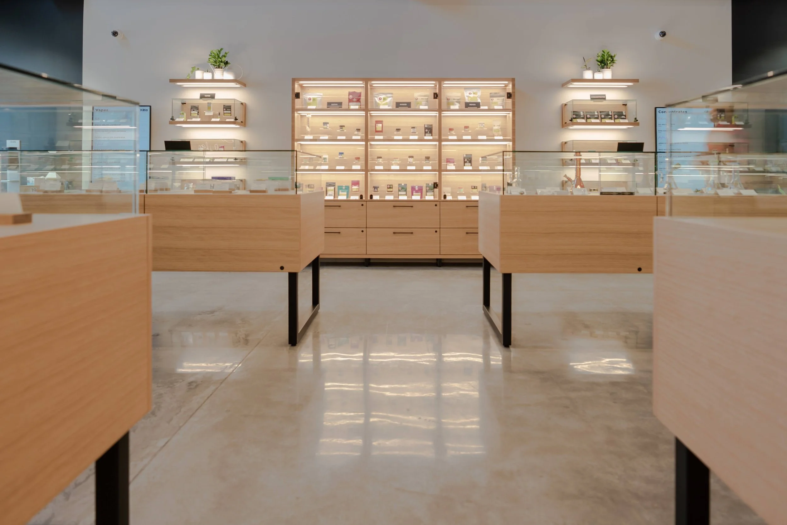 Retail interior with light oak display cases on black steel legs, glass counters and lit oak shelving behind