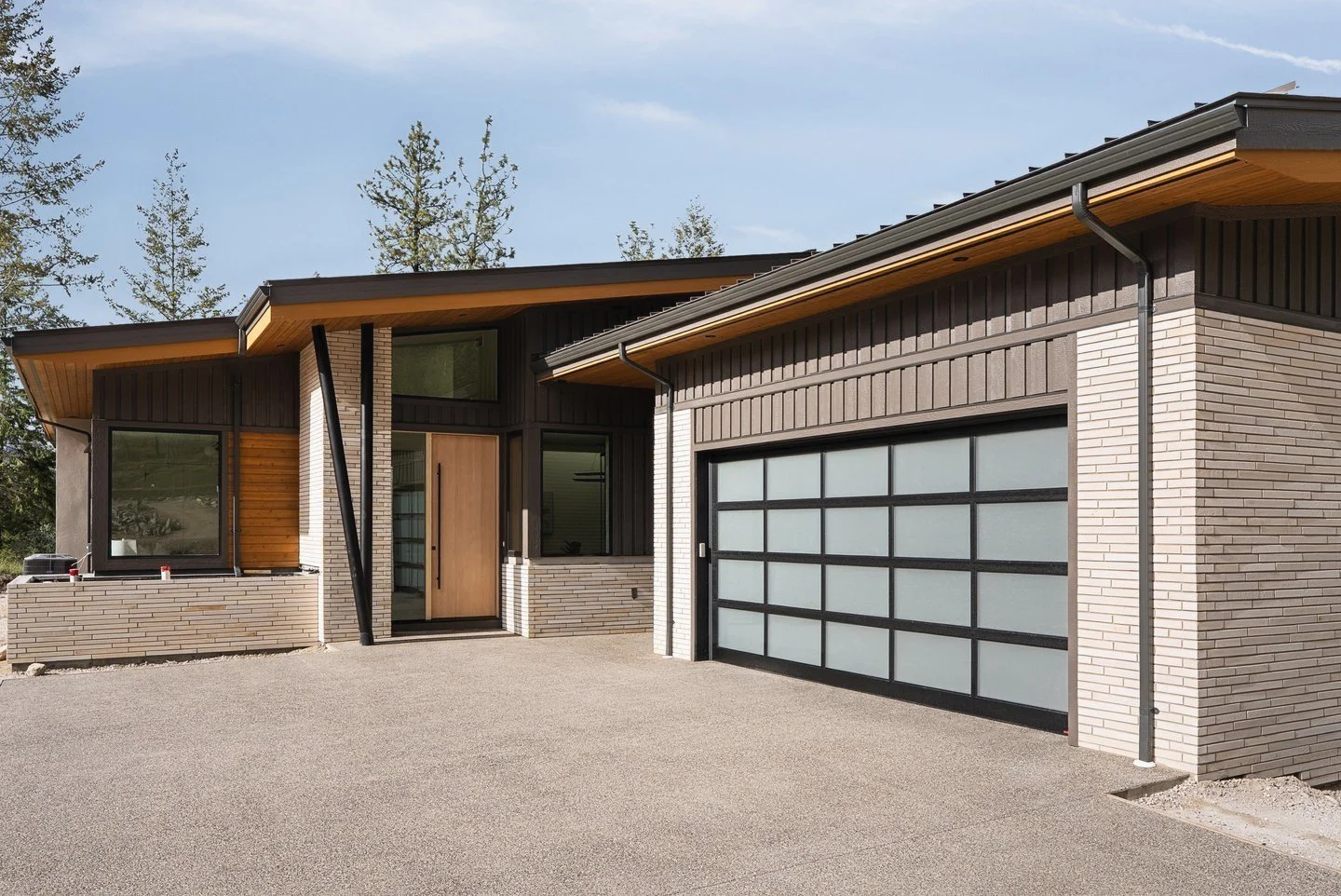 Front entry with pale brick, black siding, a wood door and a glass garage door, Fairway Rancher, Predator Ridge
