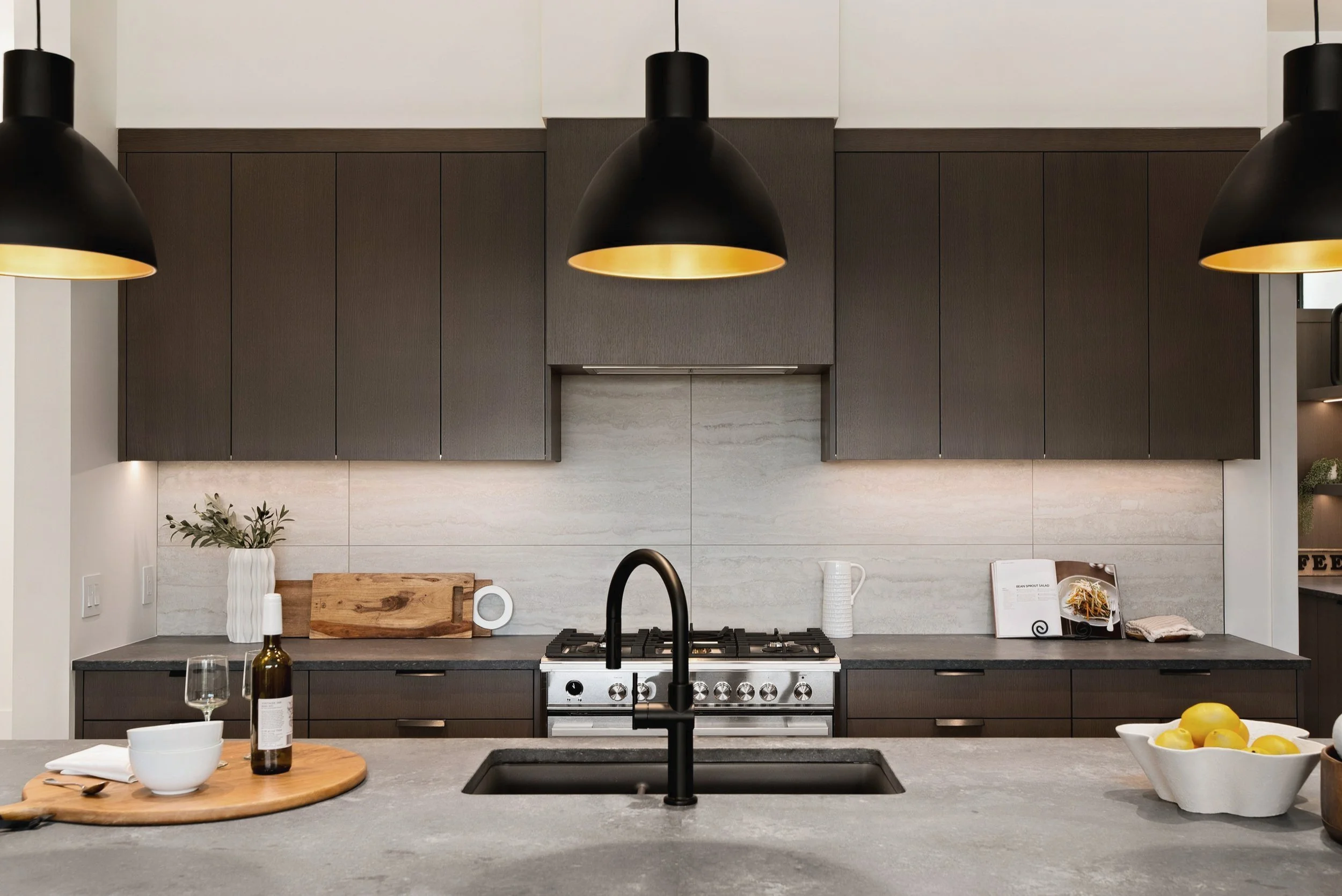 Range wall with dark wood cabinetry and black pendants over the island, Terrace House, Predator Ridge