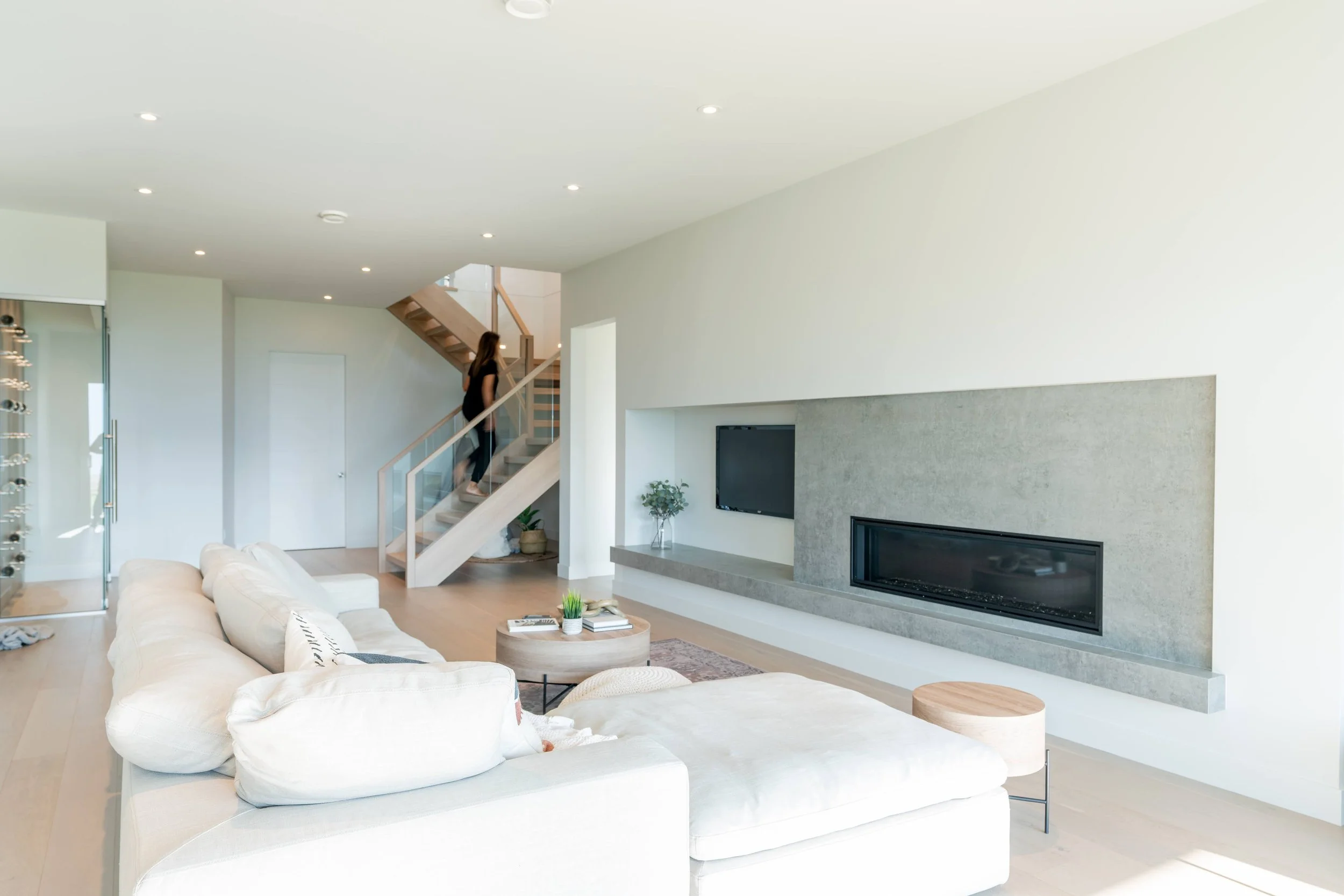 Open living room with a textured concrete-tile fireplace wall and floating staircase, Lakestone Showhome, Lake Country
