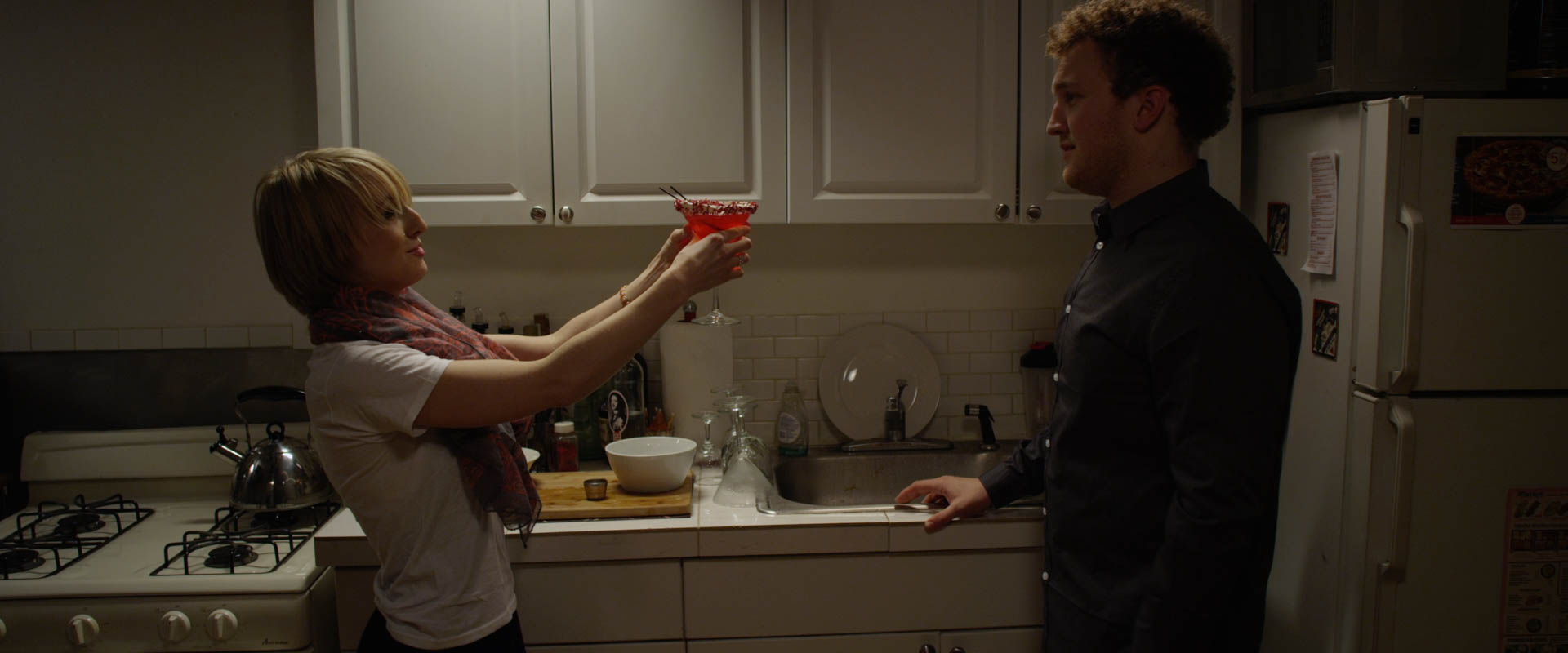 This is the scene when Luke finally tries Christelle's Velours Rouge cocktail and we start to see the connection between them forming. The great challenge of photographing this film was that the vast majority of the script takes place in this room of the apartment, and the director wanted to shoot 360 degrees around the space. It became unthinkable to try to photograph the whole film with light stands all over the place, constantly being moved around. Instead I had to devise a lighting plan that used no stands at all, but was still capable of effectively lighting the entire set, and allowed flexibility for tweaks from scene to scene. To that end, we ended up rigging an array of tungsten balanced china balls to the ceiling, as well as a number of Kino Flo fluorescent, open face, and fresnel lights along the walls above the set. This gave the director flexibility to block the scenes wherever she wanted and we never had to move lights. 