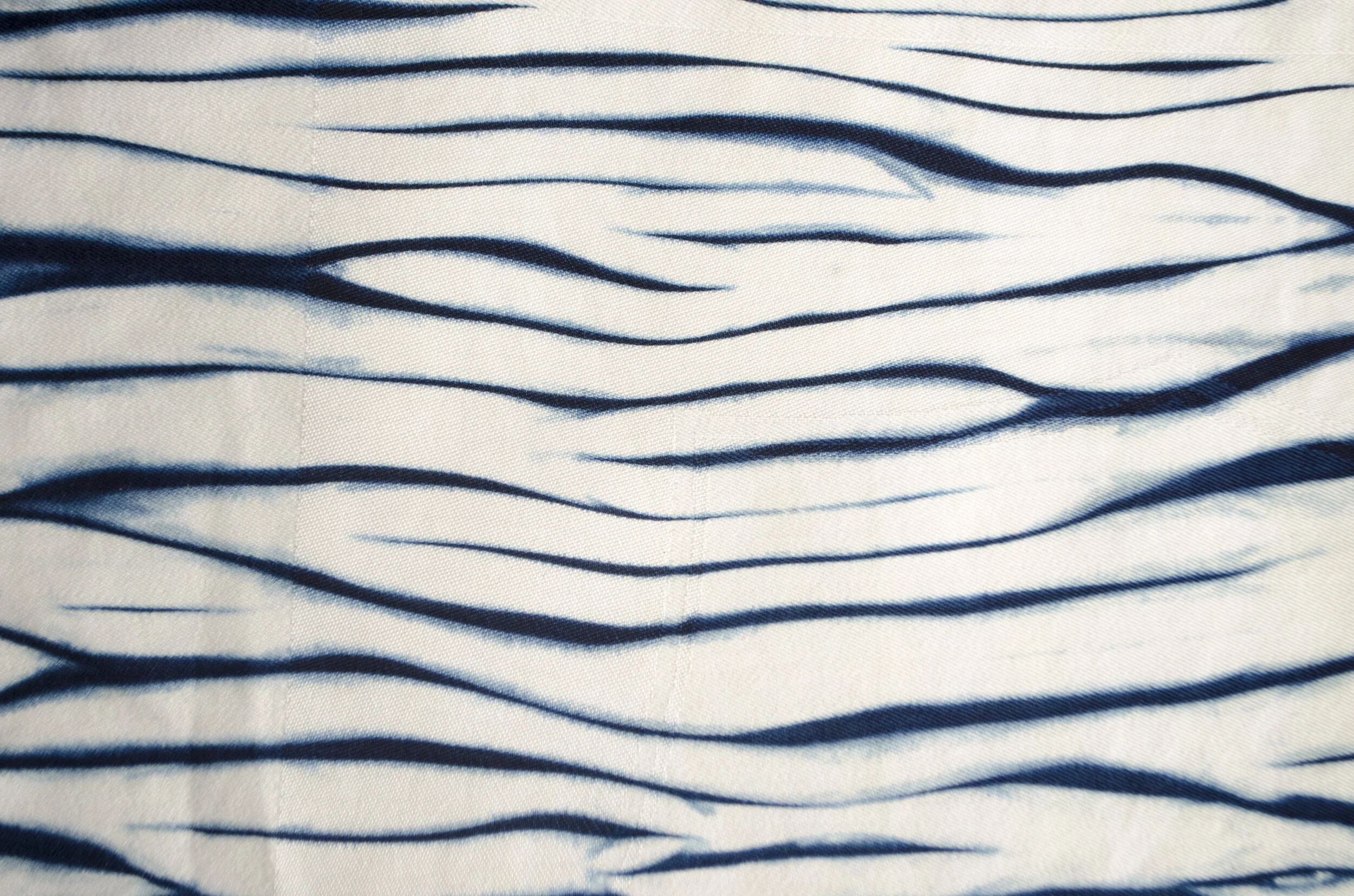 Indigo blue and white arashi shibori dyed fabric featuring wavy, diagonal pole-dyed line patterns.