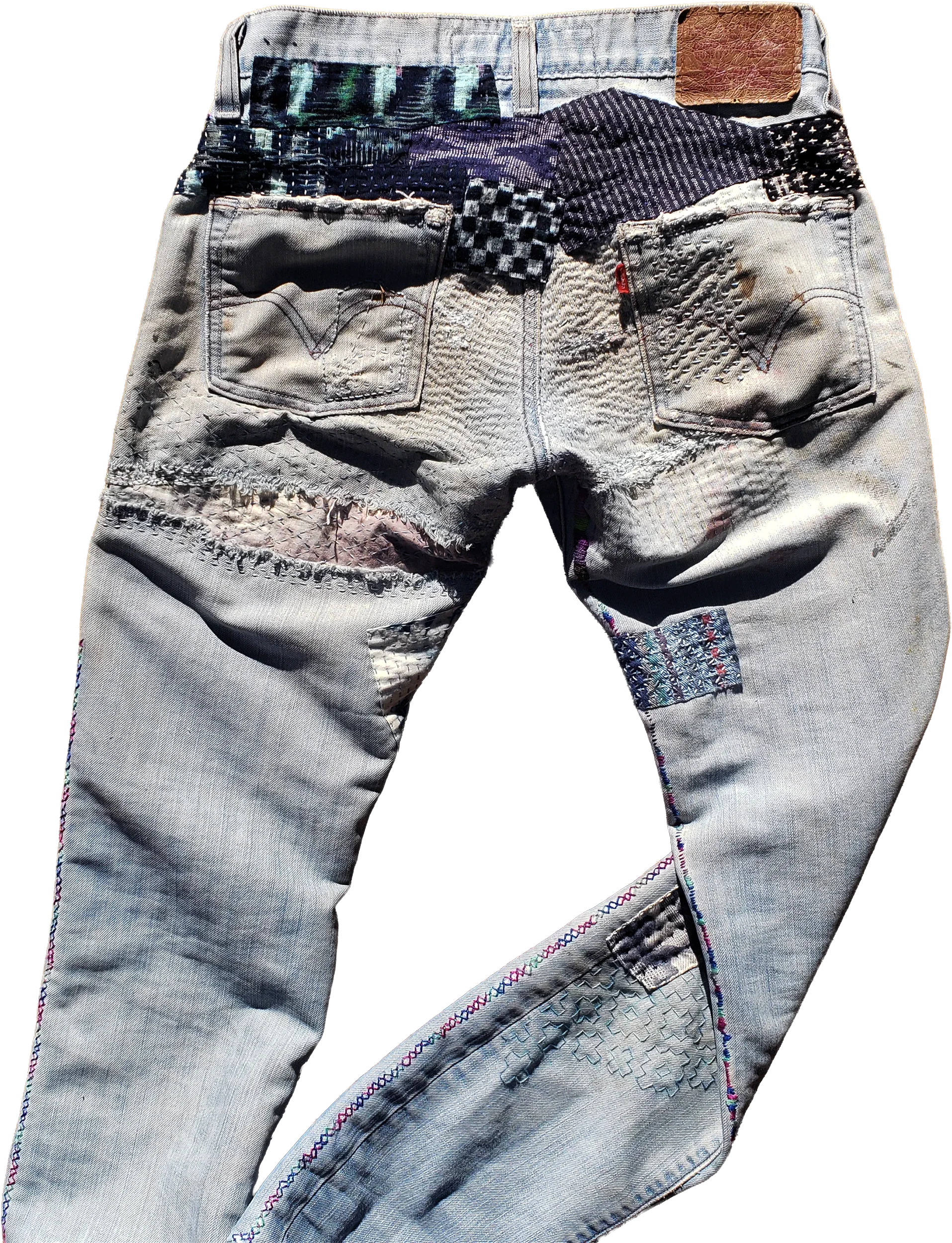 Back view of light-wash vintage Levi’s jeans featuring extensive multi-technique visible mending and hand stitching. The back yoke is heavily paneled with indigo-dyed fabric swatches, checkered textiles, and patterned patches, while dense running sti