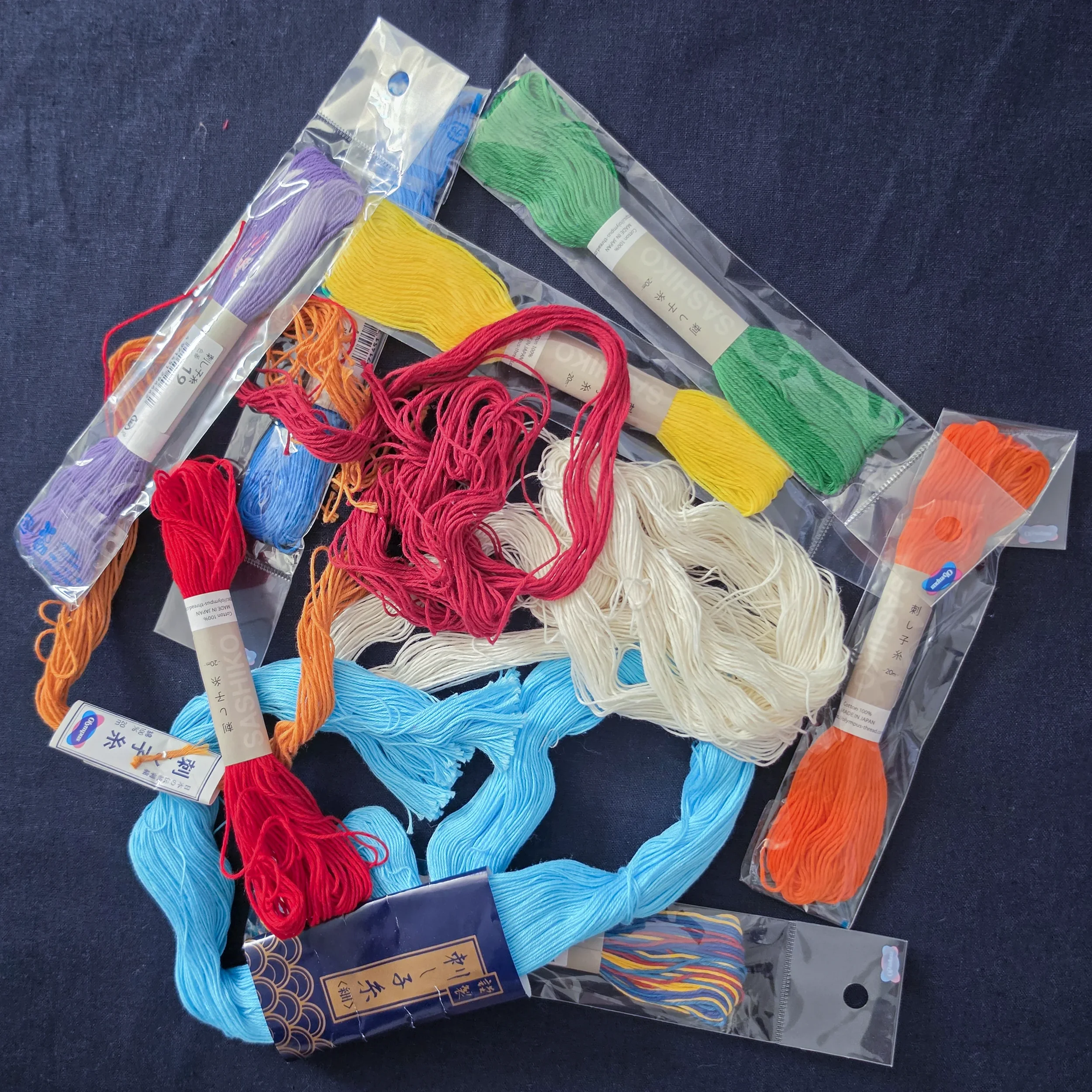 Colorful sashiko threads in packages and skeins, spread over navy fabric.