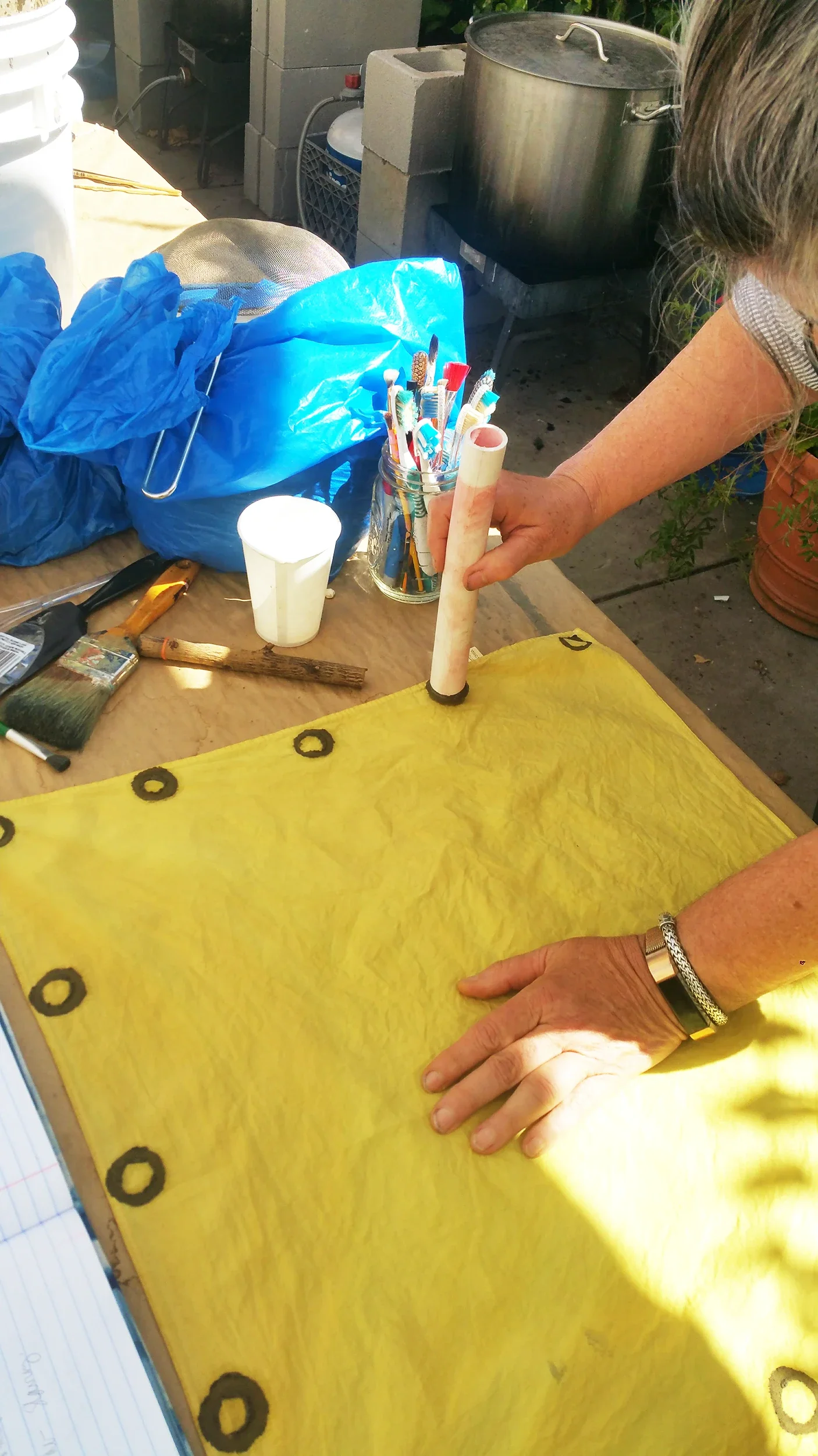 Close-up detail of Carlyn Clark applying hand-printed marks with Malian tannin-rich mud onto plant-dyed yellow cloth.