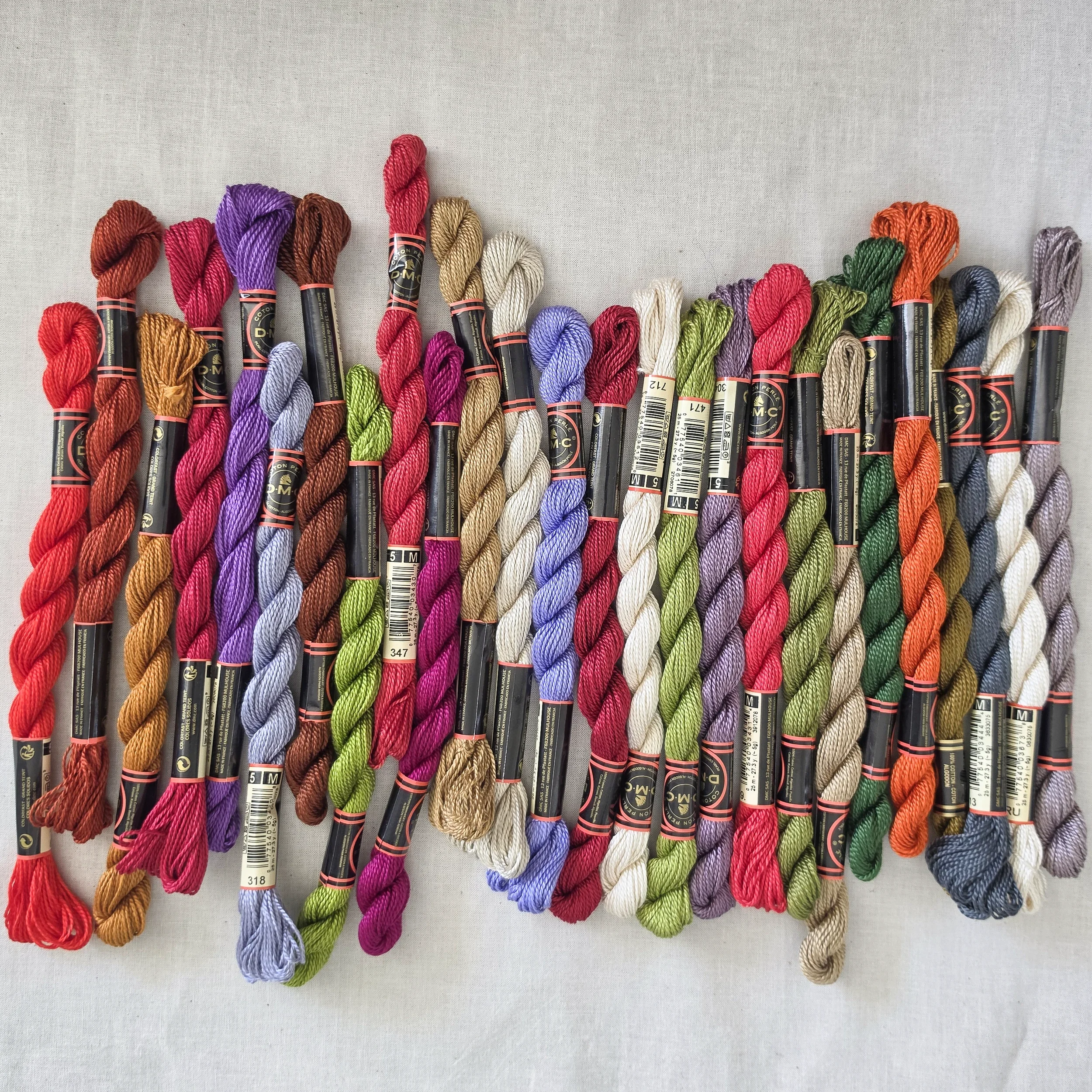 Skeins of DMC size 5 pearl cotton in a wavy row of bright and muted colors.