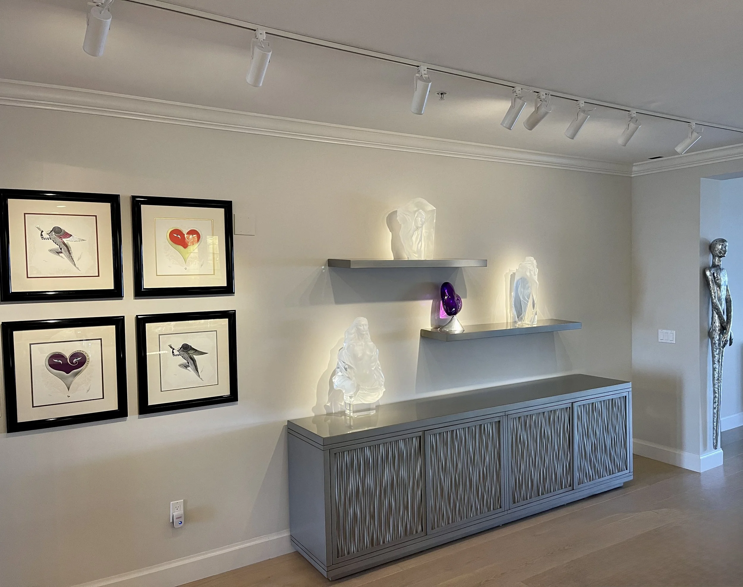 White track lighting highlighting fine artwork framing and glass sculptures on floating shelves in a luxury Fort Myers Florida home interior
