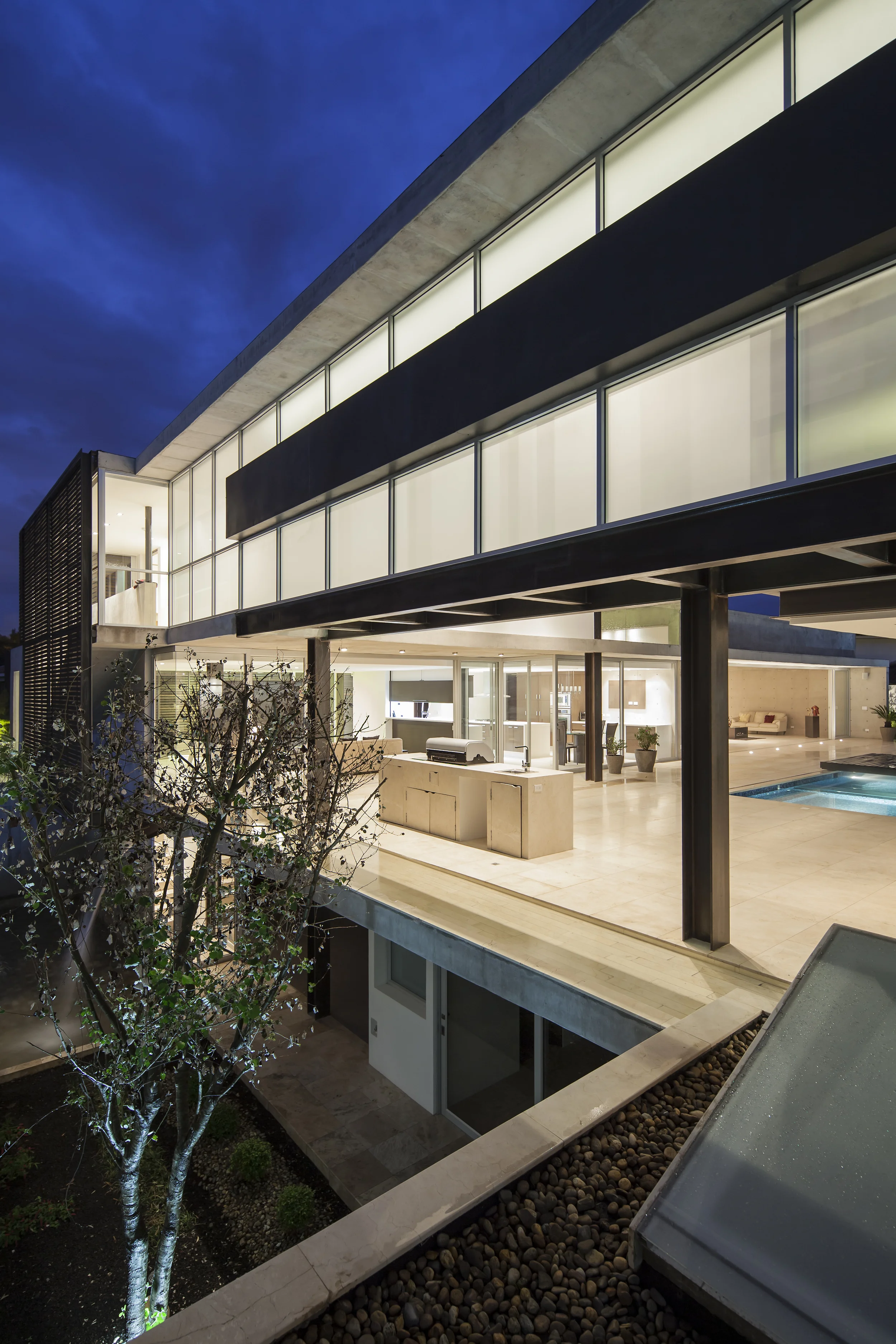 Casa L6, vista fachada lateral, patio en el nivel -1, porche con bbq y corredor de vidrio en la planta alta. Diseñado por Endara Arquitectos.