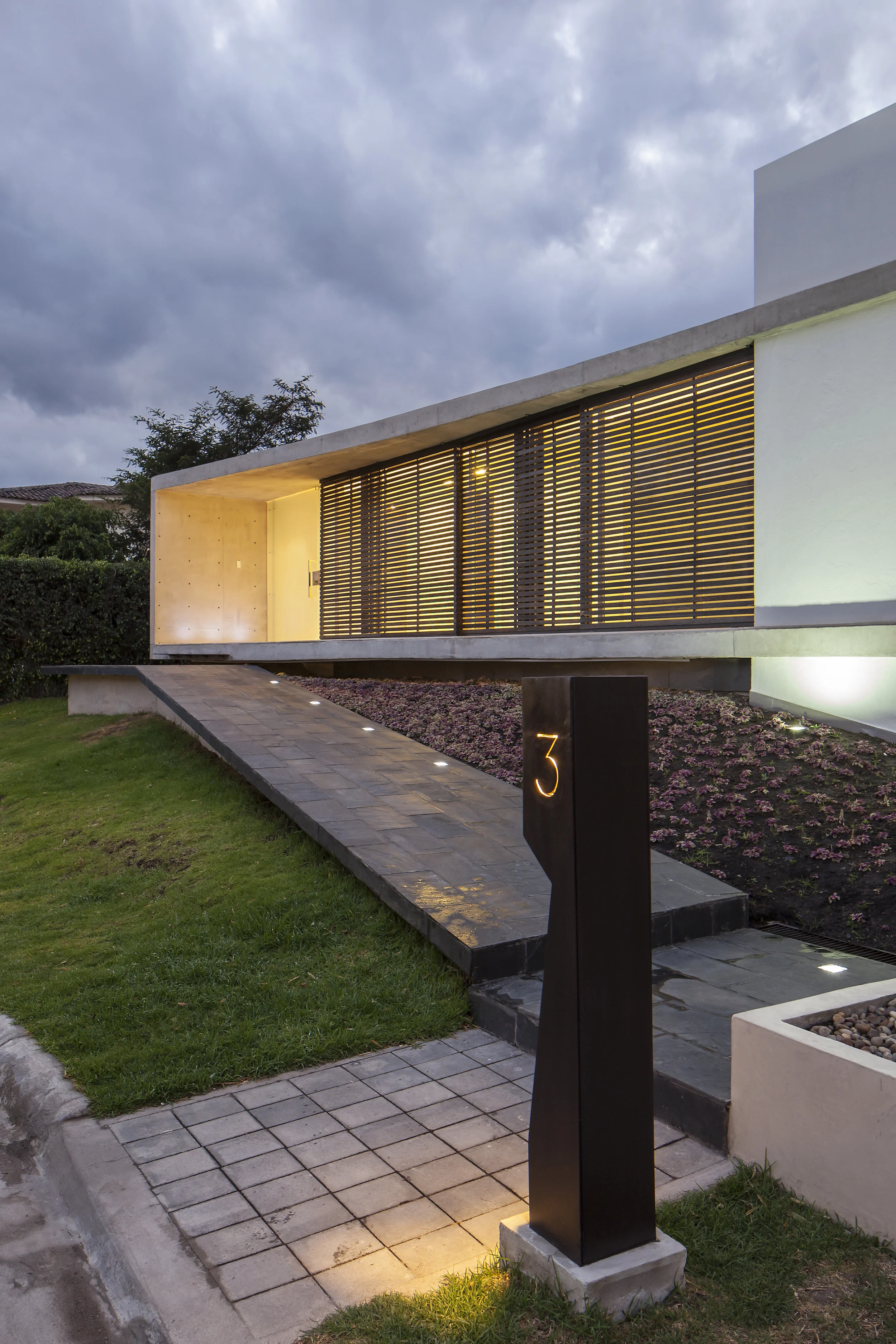 Casa L6, acceso peatonal principal, volumen de hormigón elevado que llega por una rampa. Diseñada por Endara Arquitectos
