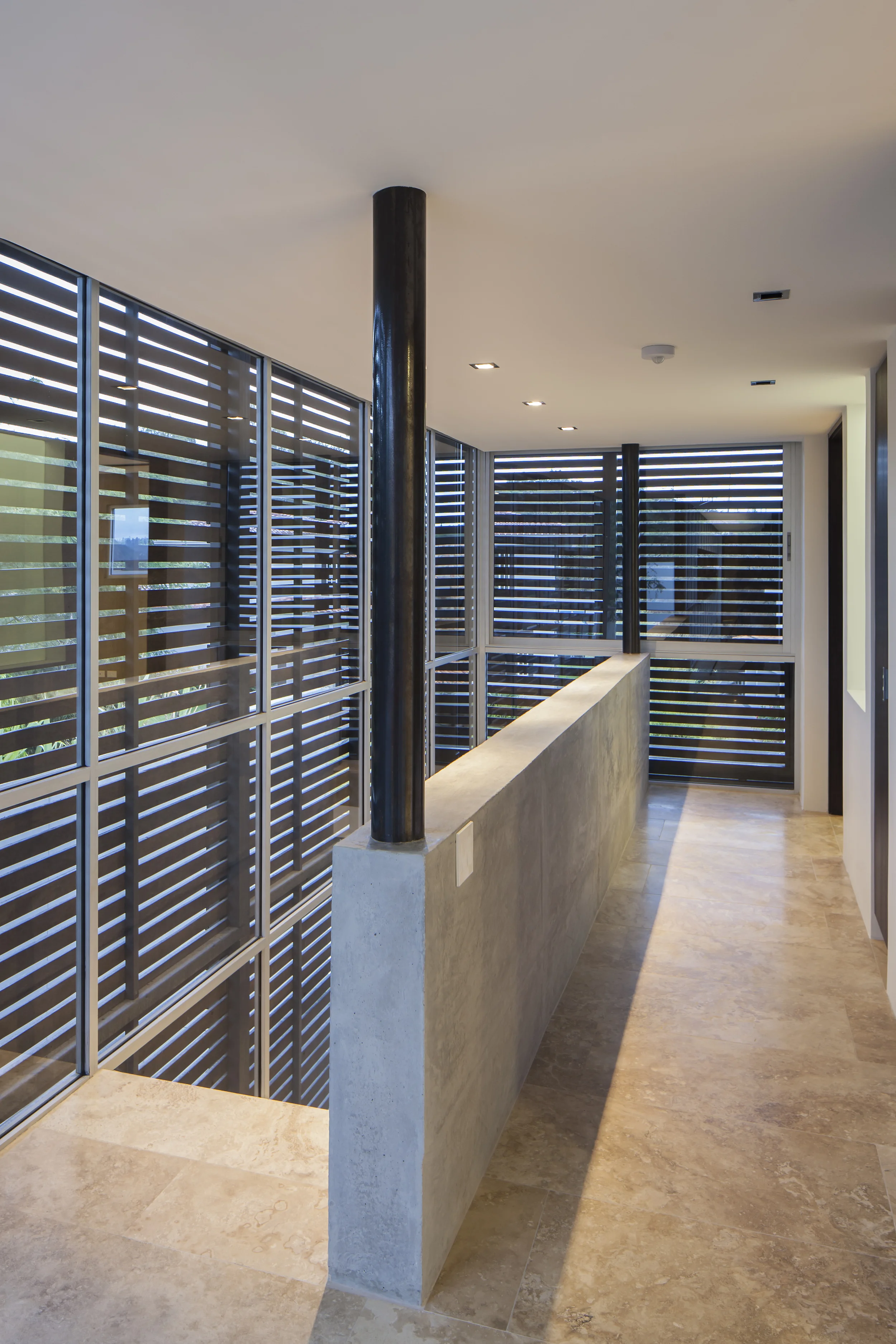 Casa L6, gradas y corredor llegando al segundo piso, con columnas redondas, hormigón y pisos de porcelanato. Diseñado por Endara Arquitectos.