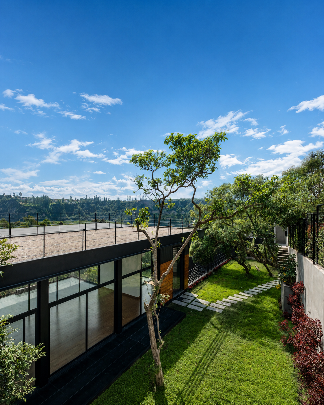Vista elevada del patio posterior de Pillagua Barranco, con jardín, senderos y espacios interiores conectados mediante grandes superficies acristaladas. Proyecto de ENDARA ARQUITECTOS en Cumbayá.