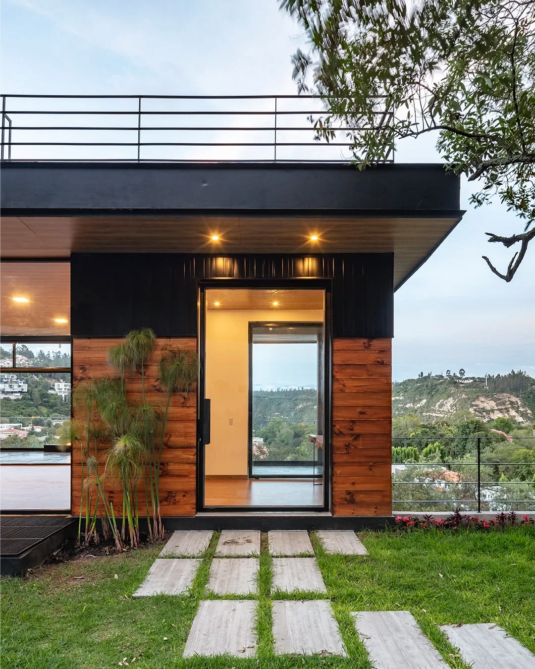 Acceso principal a una de las tres viviendas independientes de Pillagua Barranco, con revestimiento de madera, acero y vidrio y vistas hacia el paisaje de Cumbayá. Proyecto diseñado por ENDARA ARQUITECTOS.