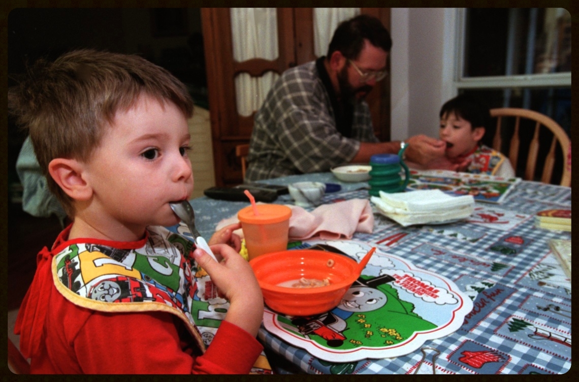 James eat his breakfast while their father feed Mark.