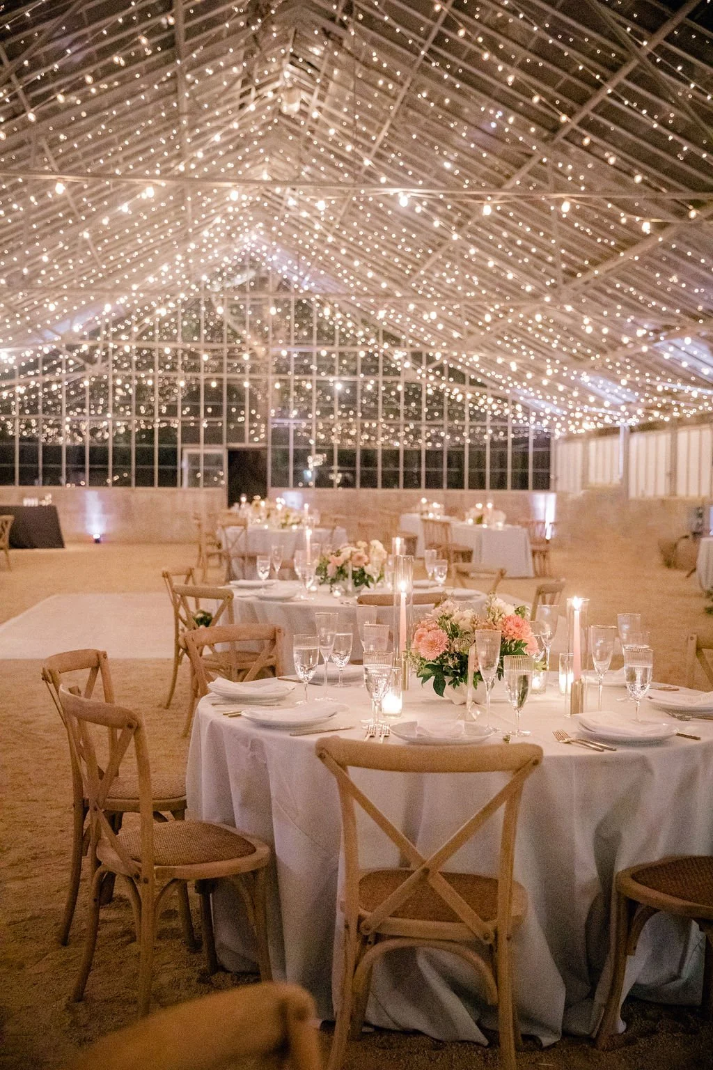 Evening wedding reception at Dos Pueblos Orchid Farm featuring glowing string lights, round tables, and an intimate greenhouse atmosphere.