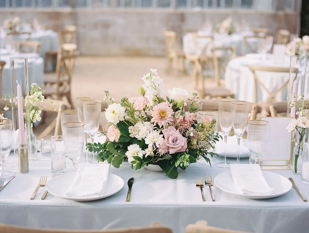 Romantic wedding reception table at Dos Pueblos Orchid Farm with pastel floral centerpiece, glassware, and neutral linens in the greenhouse venue.