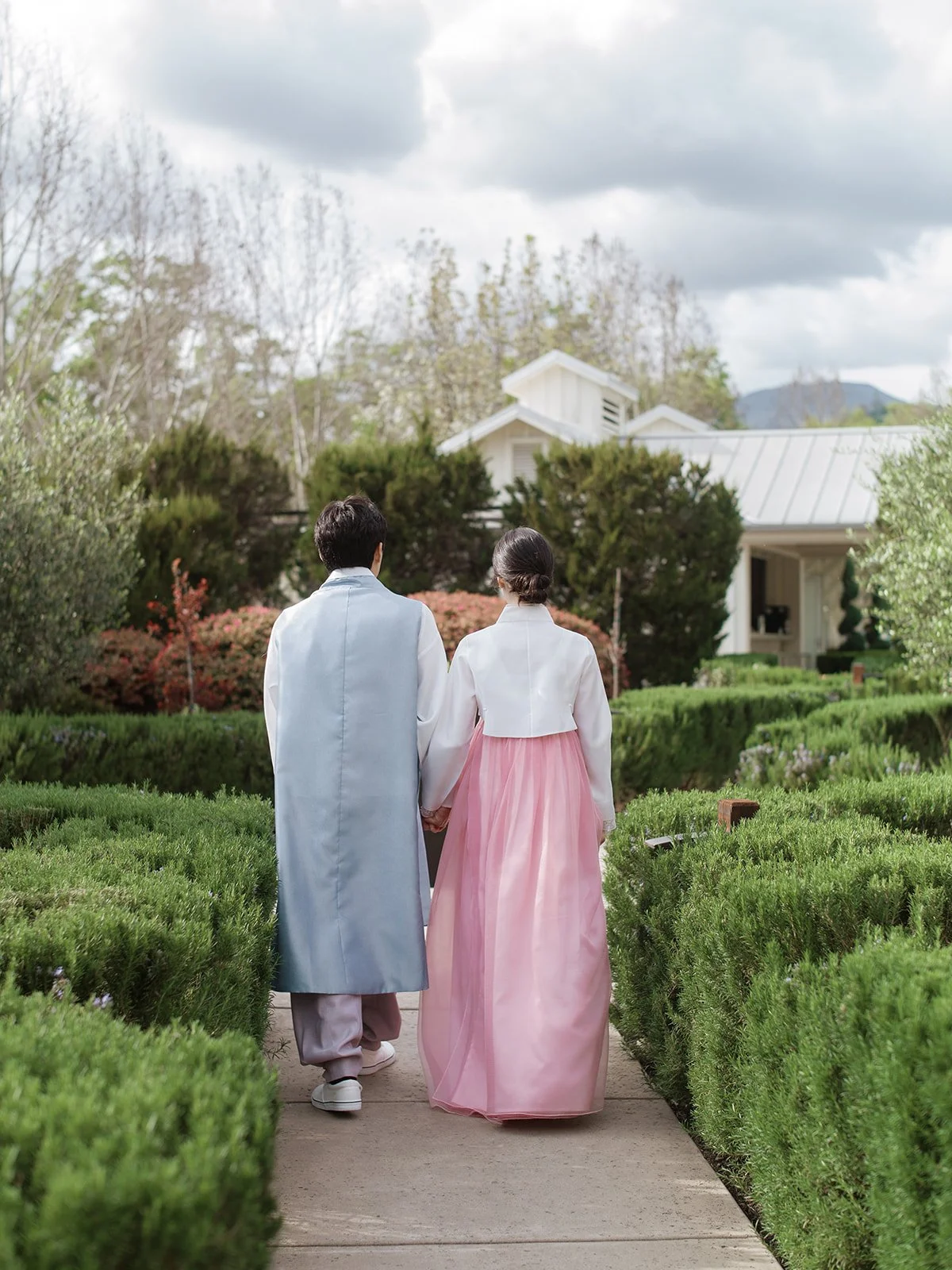 Wedding couple wearing traditional Korean hanbok walking hand in hand through the garden paths at Solage Calistoga.