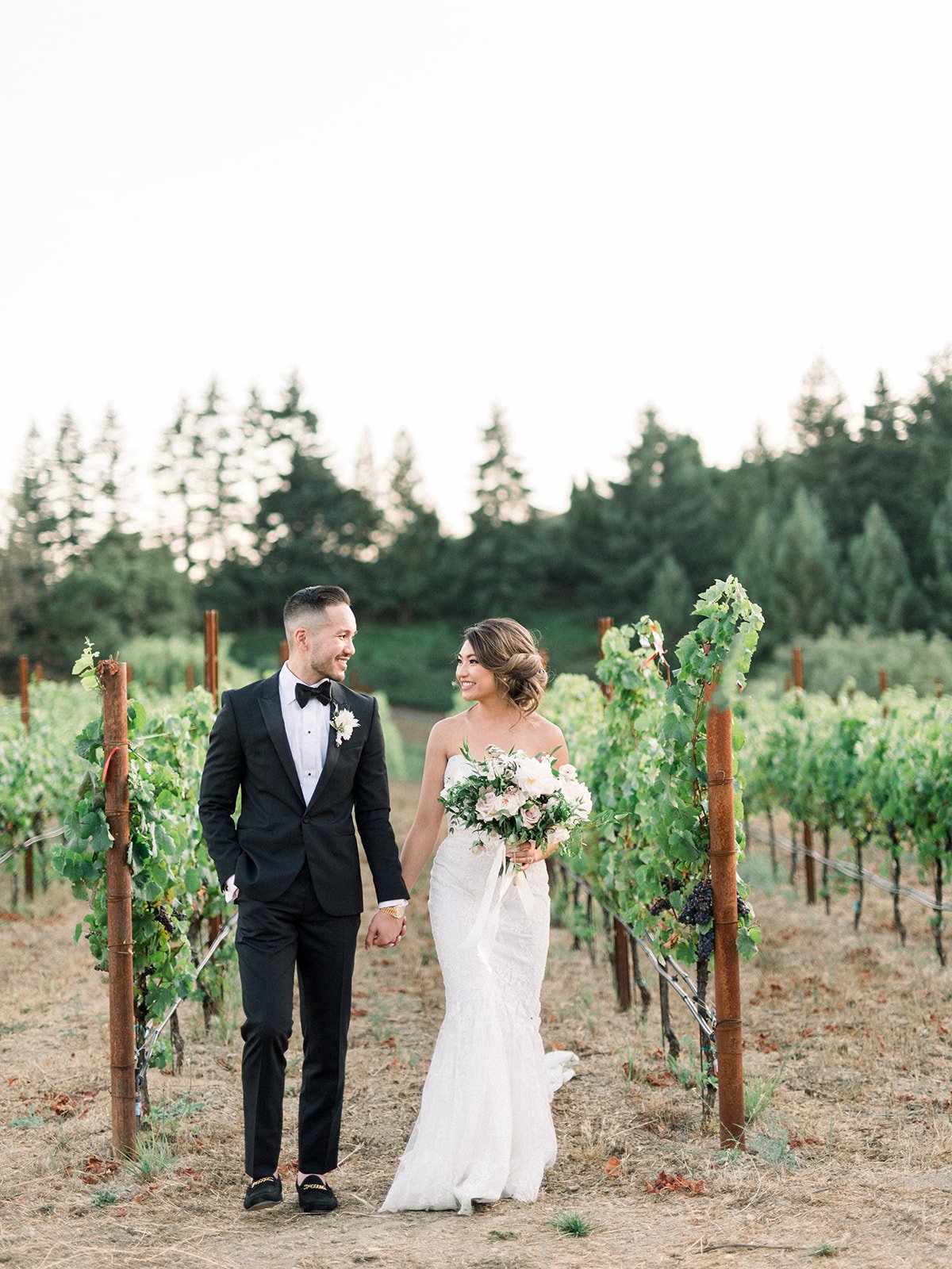 Bride and groom walking hand in hand through vineyard rows at Thomas Fogarty Winery in Woodside, California.