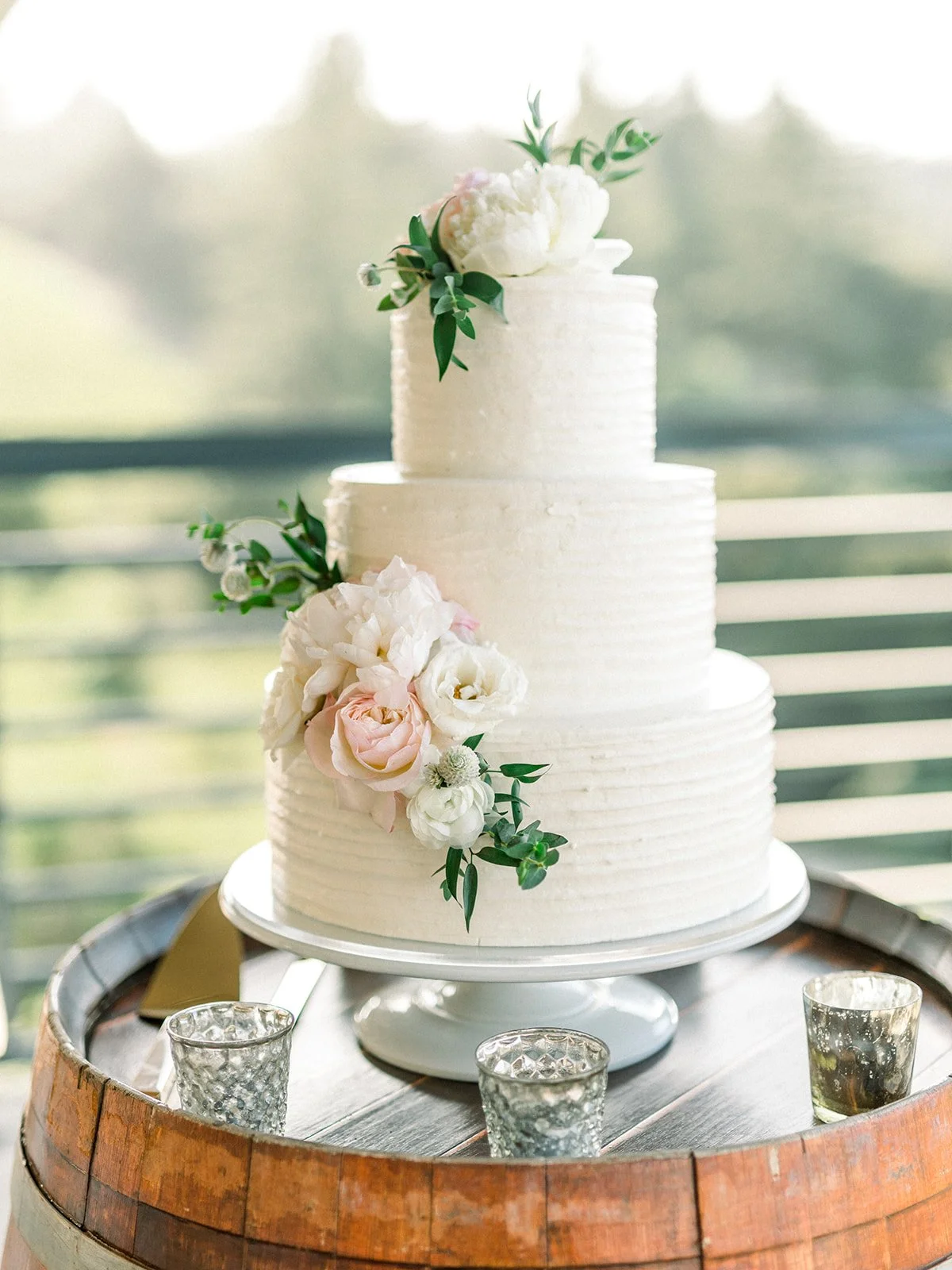 Three-tier white buttercream wedding cake with floral accents at a Thomas Fogarty Winery wedding.