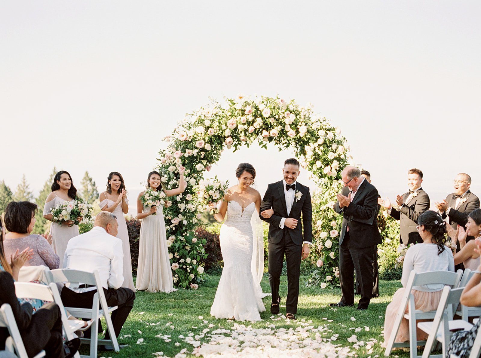 Bride and groom walk down the aisle after their outdoor wedding ceremony beneath a floral arch at Thomas Fogarty Winery.