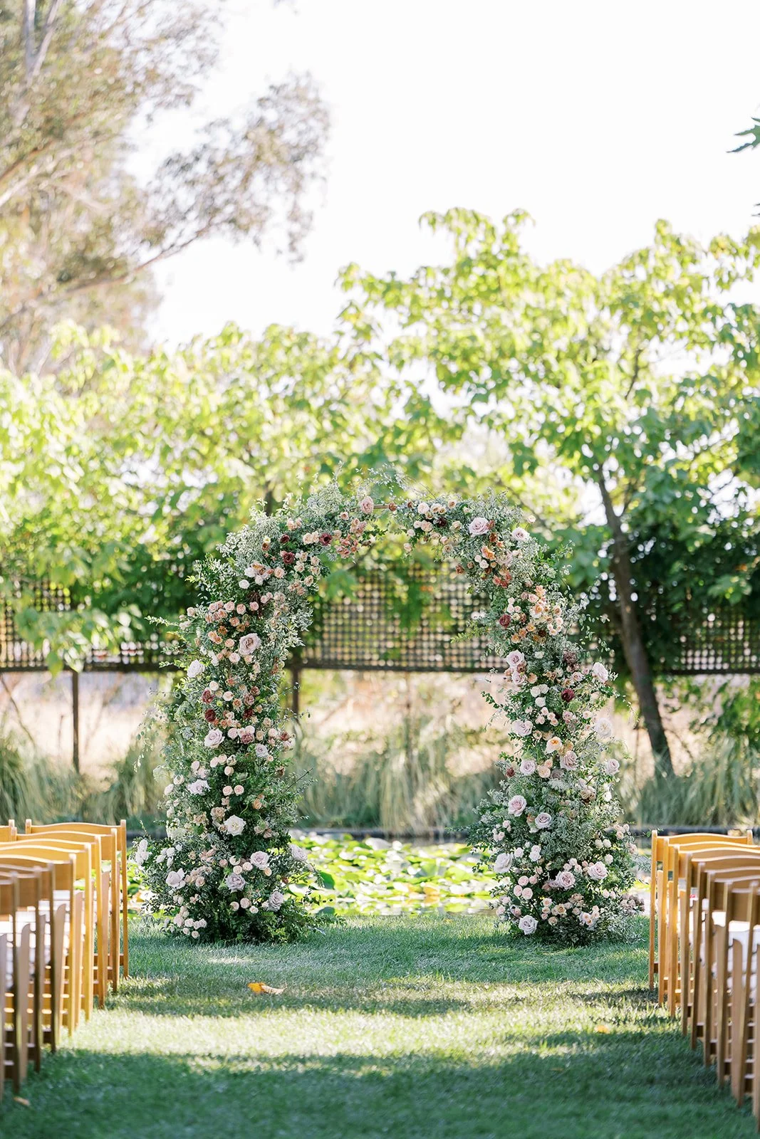 Romantic outdoor wedding ceremony at Cornerstone Gardens featuring a lush floral arch with blush and ivory roses.