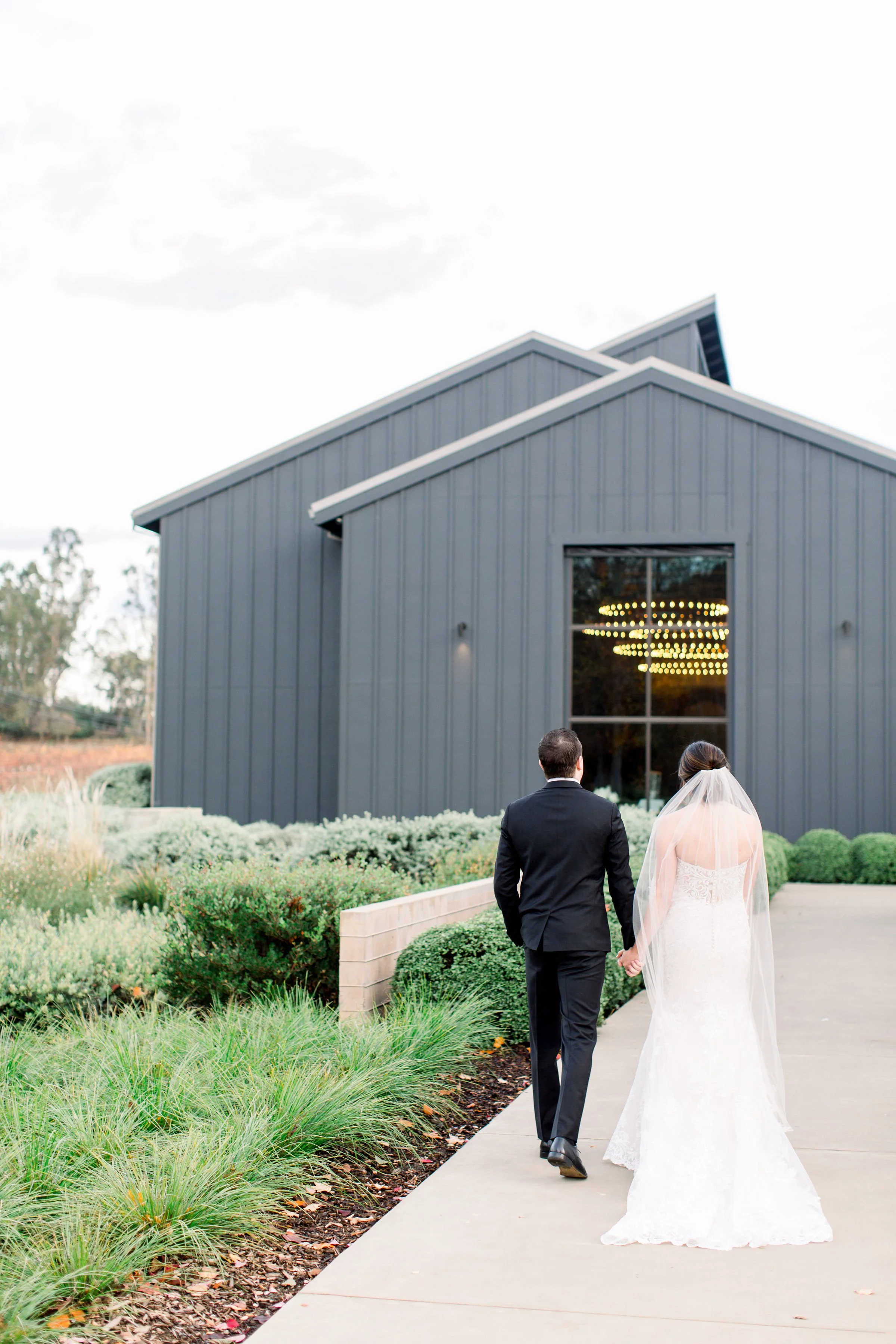 Bride and groom walking hand-in-hand toward the black barn at Brasswood Estate during their Napa Valley wedding.