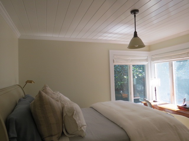 The second bedroom, the smaller, yearned for something a little different. This bedroom faces the back of the house with its little herb garden, and slate patio enclosure. The room seemed to beg for a contrapuntal statement, a place of peace all its own yet somehow more grounded in earth tones. After painting a lumber yard’s worth of small wood squares with all manner of kindred colors, all from Farrow & Ball, I came up with the funnily named Clunch, a hue that harkens to an old world feeling of weathered parchment, yet with a modern character. It’s both restful and has a touch art house cool. I wanted some texture too, so I had the ceiling done in wood plank, each about 4 inches wide, then painted them, you guessed it, All White, to lend the ceiling and trim the same glossy counterbalance to the elegant whimsy of Clunch. It works so well that the room looks both modern and ancient; it’s become both writing room and a wonderful place for naps for anyone who needs one. Libeco bed linens stand out in pale relief to the saturated wall color, and a satin-white glass lamp overhead makes a lovely compliment, on or off.