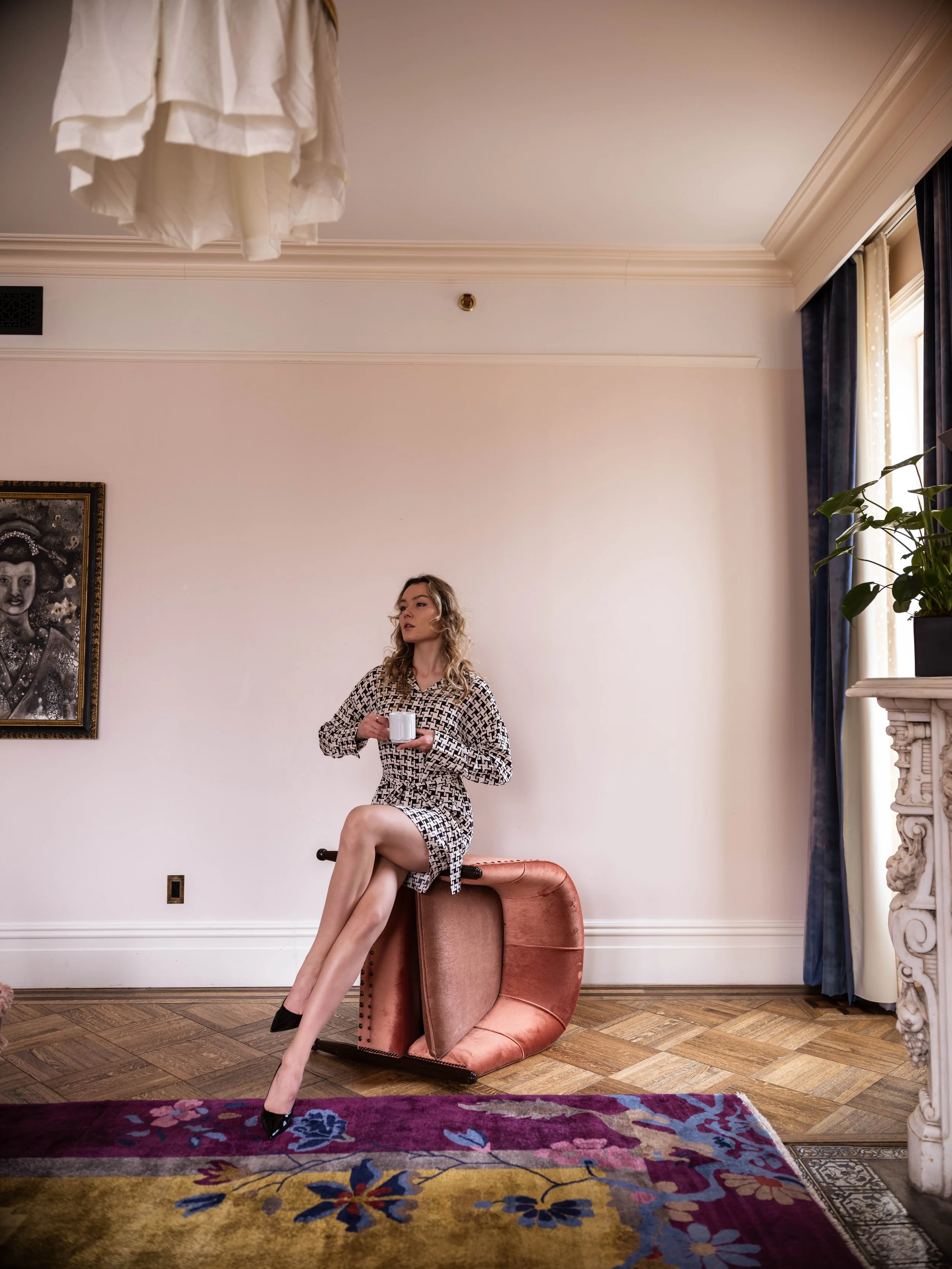Anastasiia sitting cross-legged on the sideways coral chair with a cup