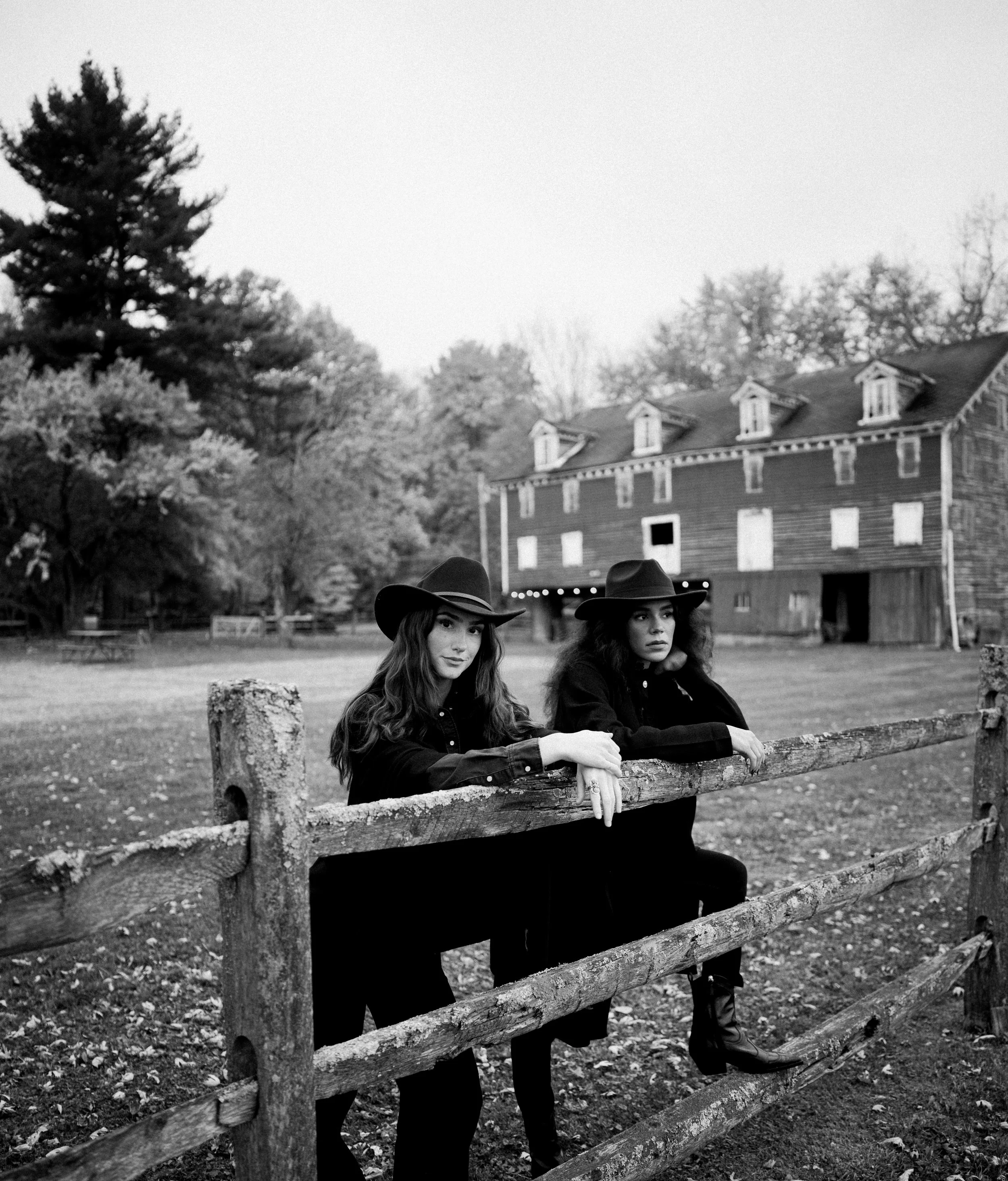 Two cowgirls leaning on a split-rail fence
