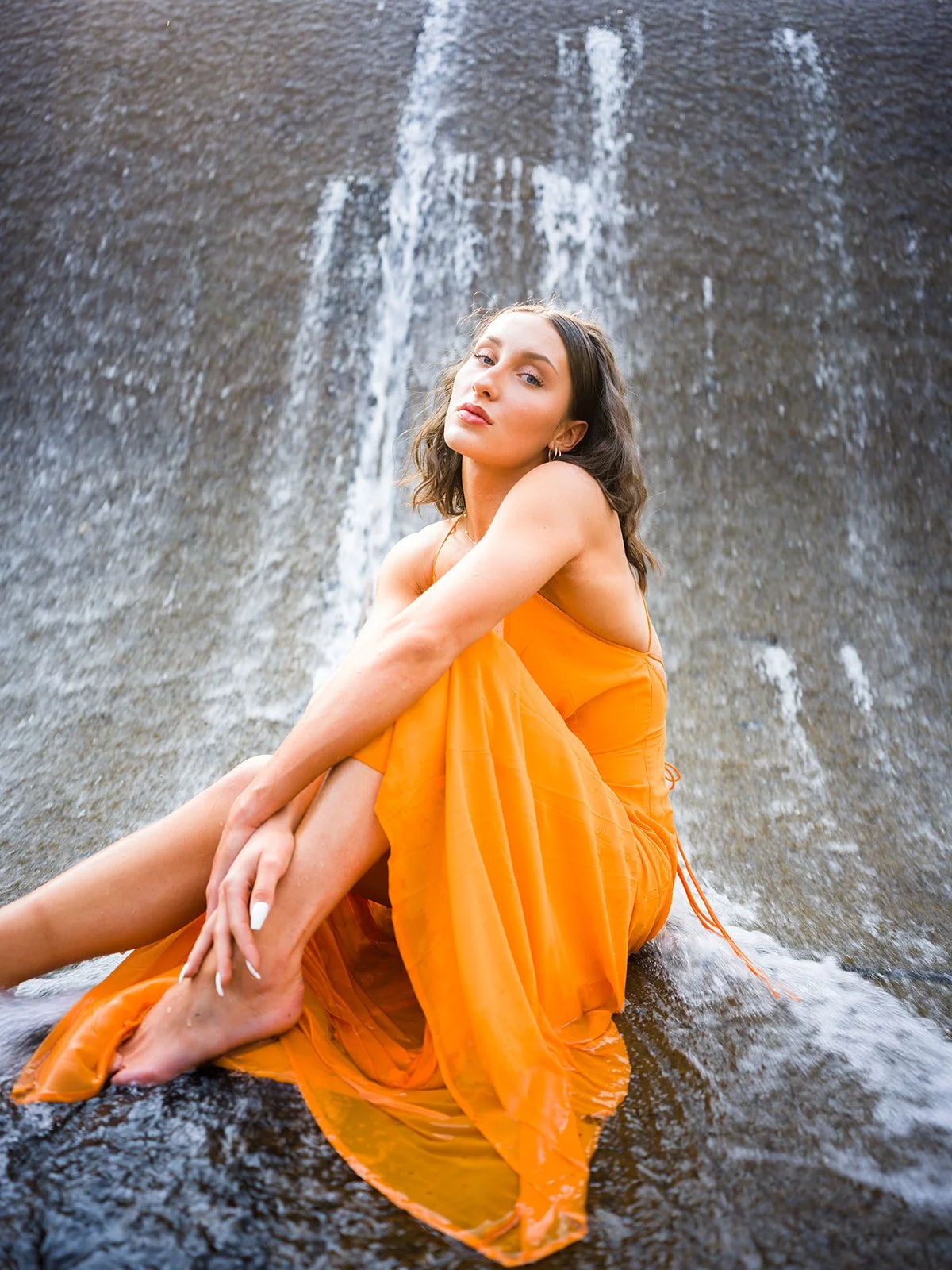Seated portrait in an orange dress beneath falling water